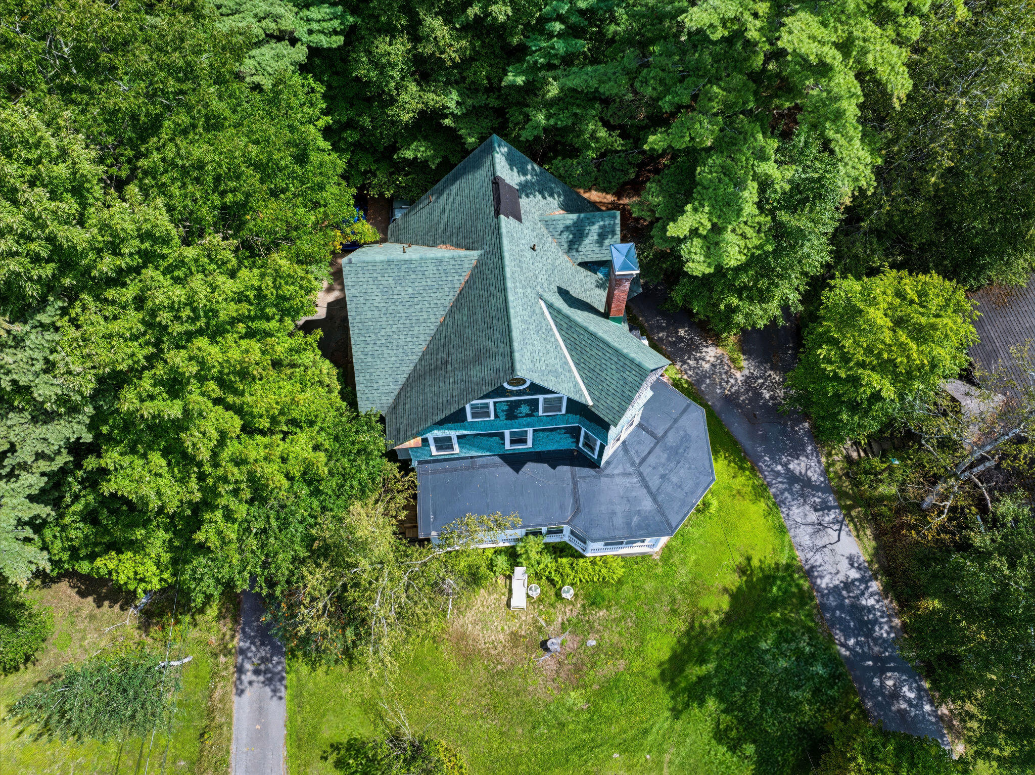 Aerial view of a home with a multi-gabled roof, screened porch, and wooded grounds.