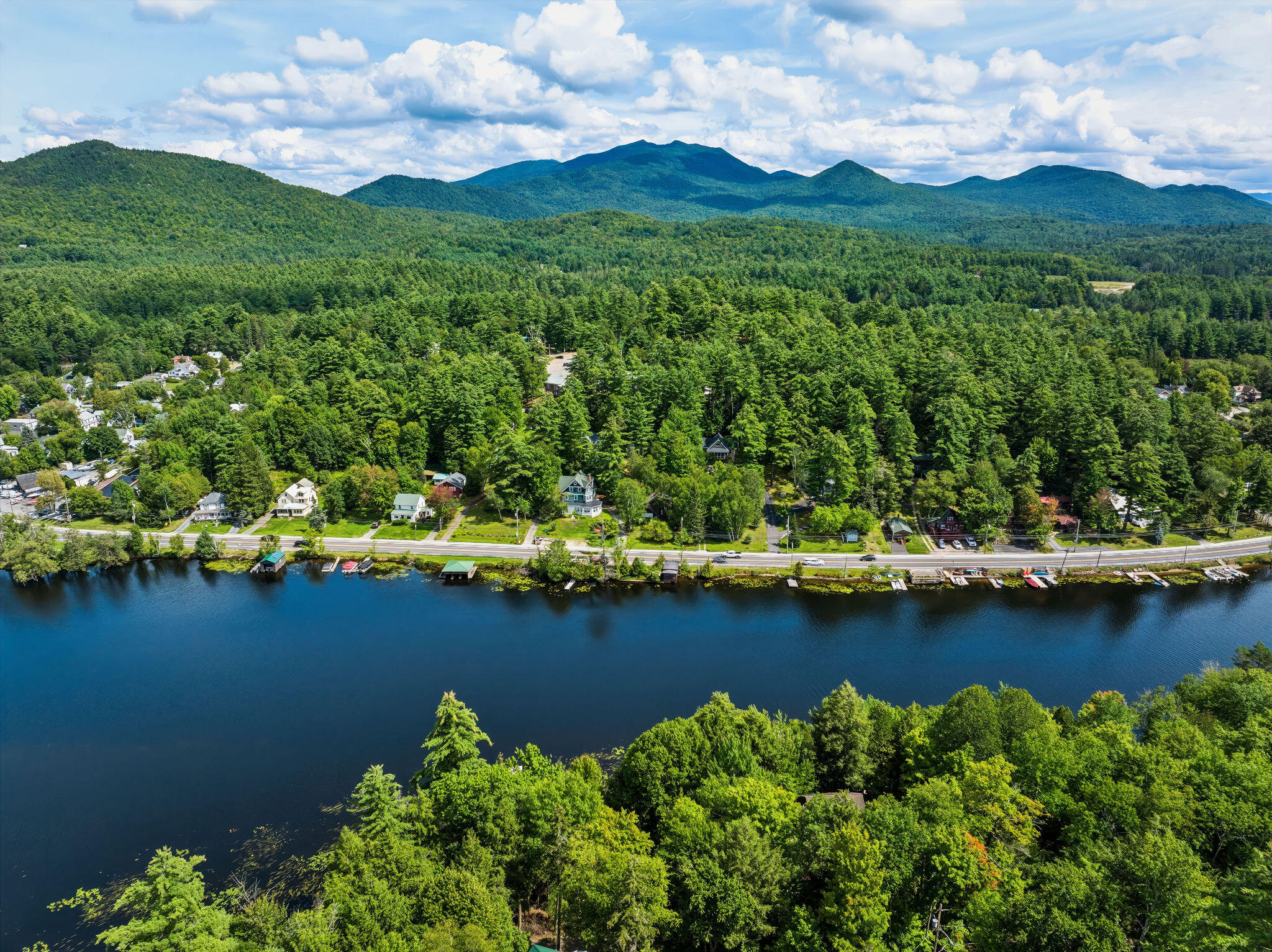 Aerial view of lakeside homes and docks, backed by dense forest and mountain ridges.