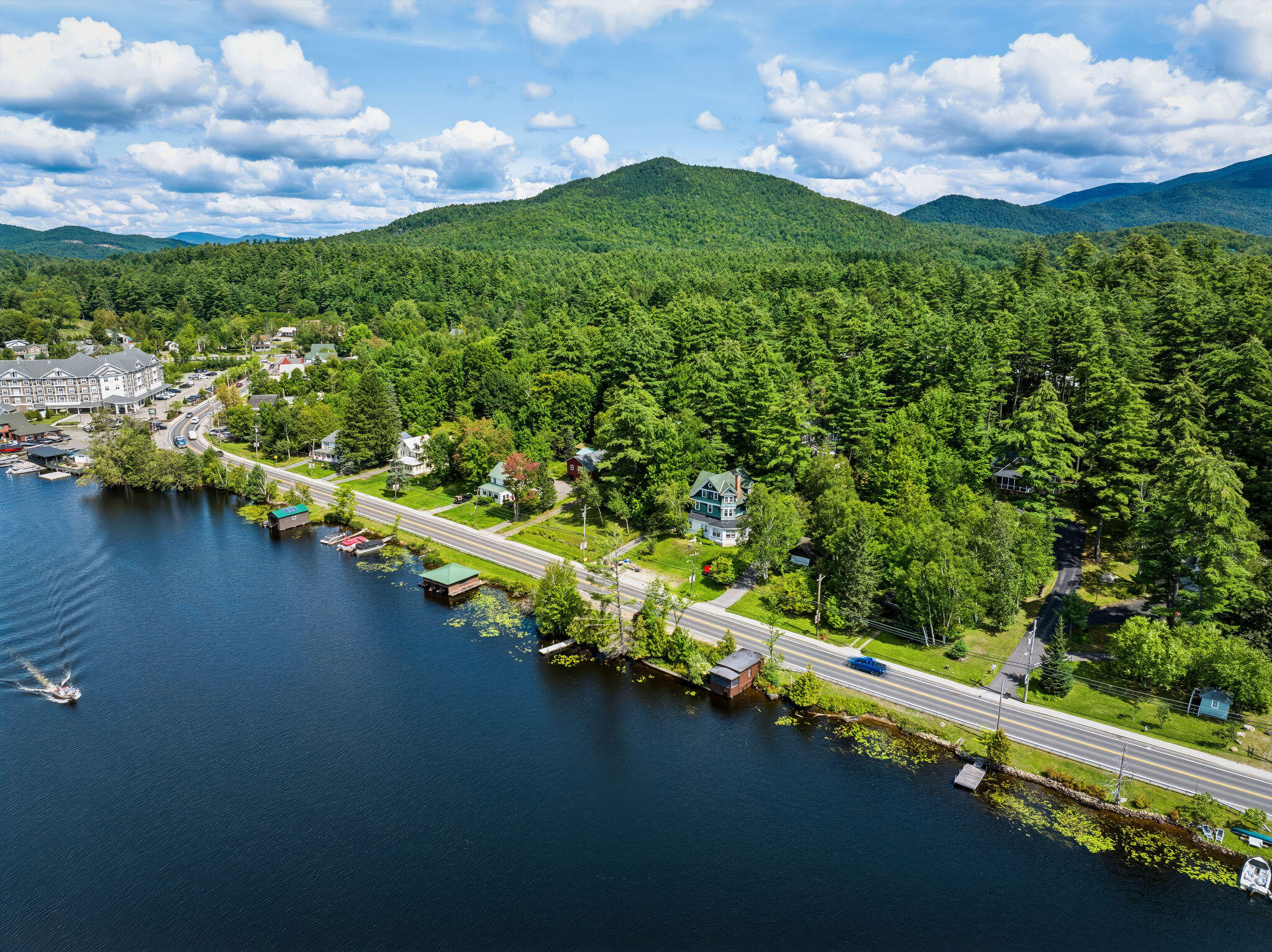 Aerial view of lakeside homes and docks along a wooded shore, with mountains beyond.
