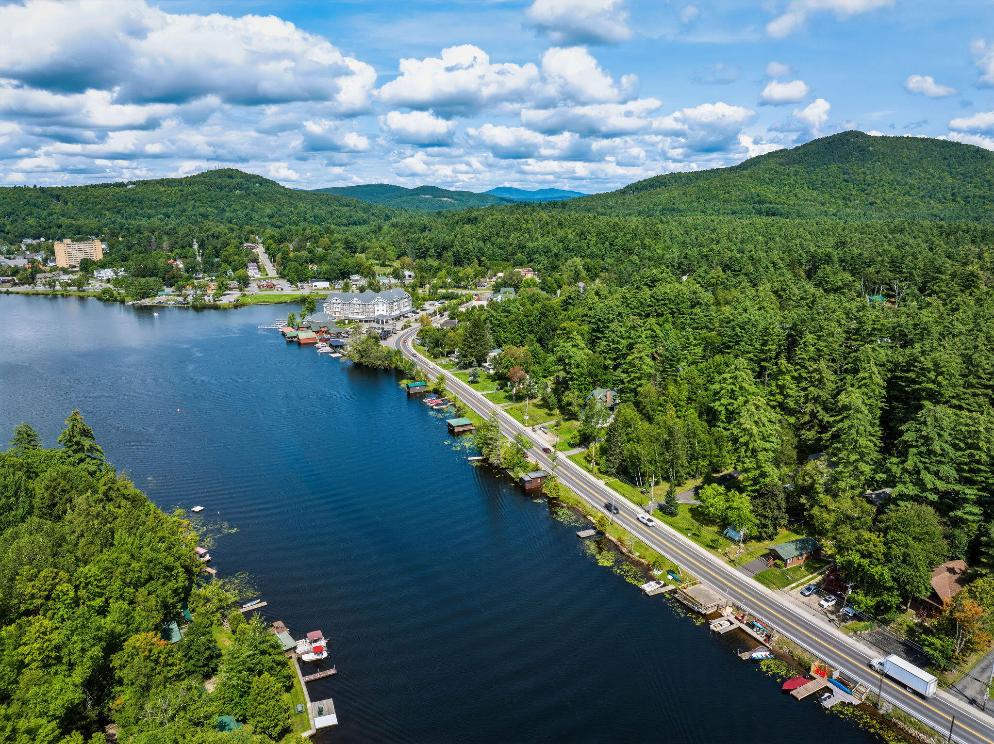 Aerial view of a lakeside town, with shoreline docks, a curving road, and forested hills.