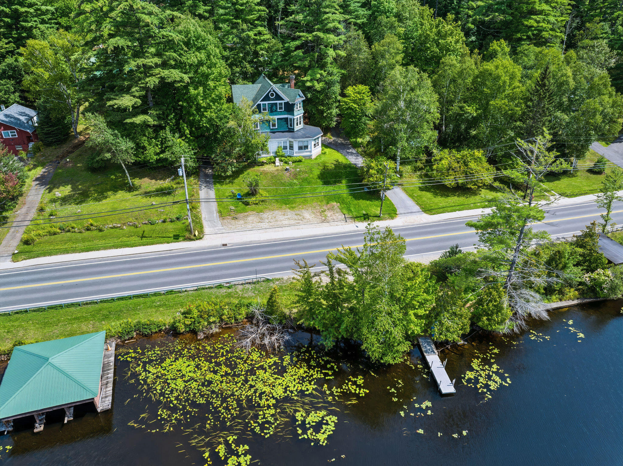 Aerial view of a wooded waterfront home with a dock and covered lakeside structure.