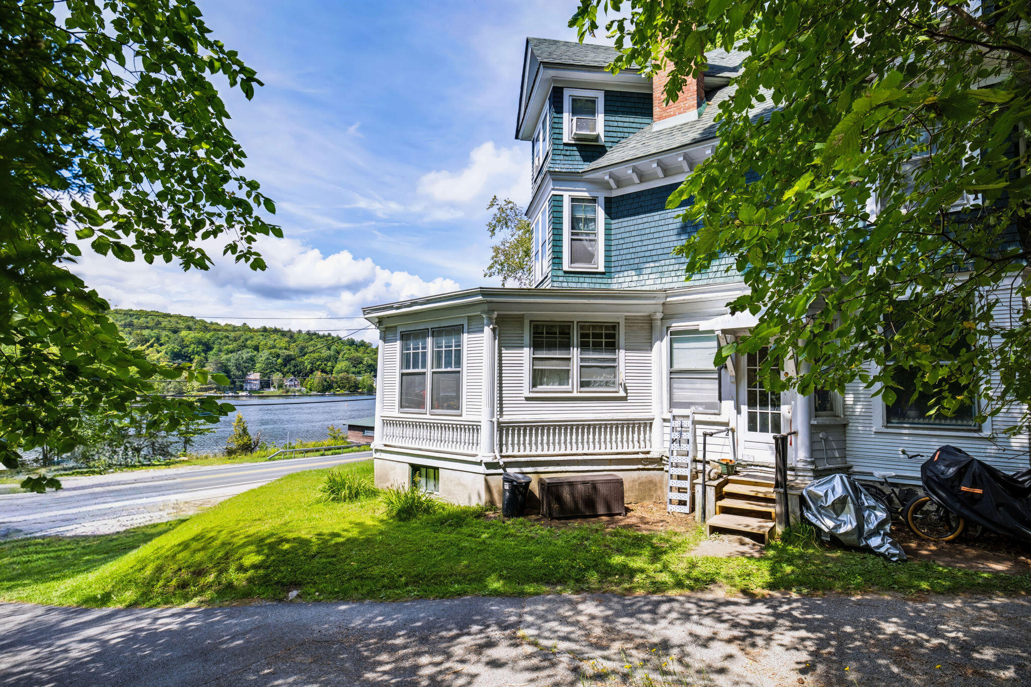 Blue-and-white shingled house beside a lake, framed by leafy trees.