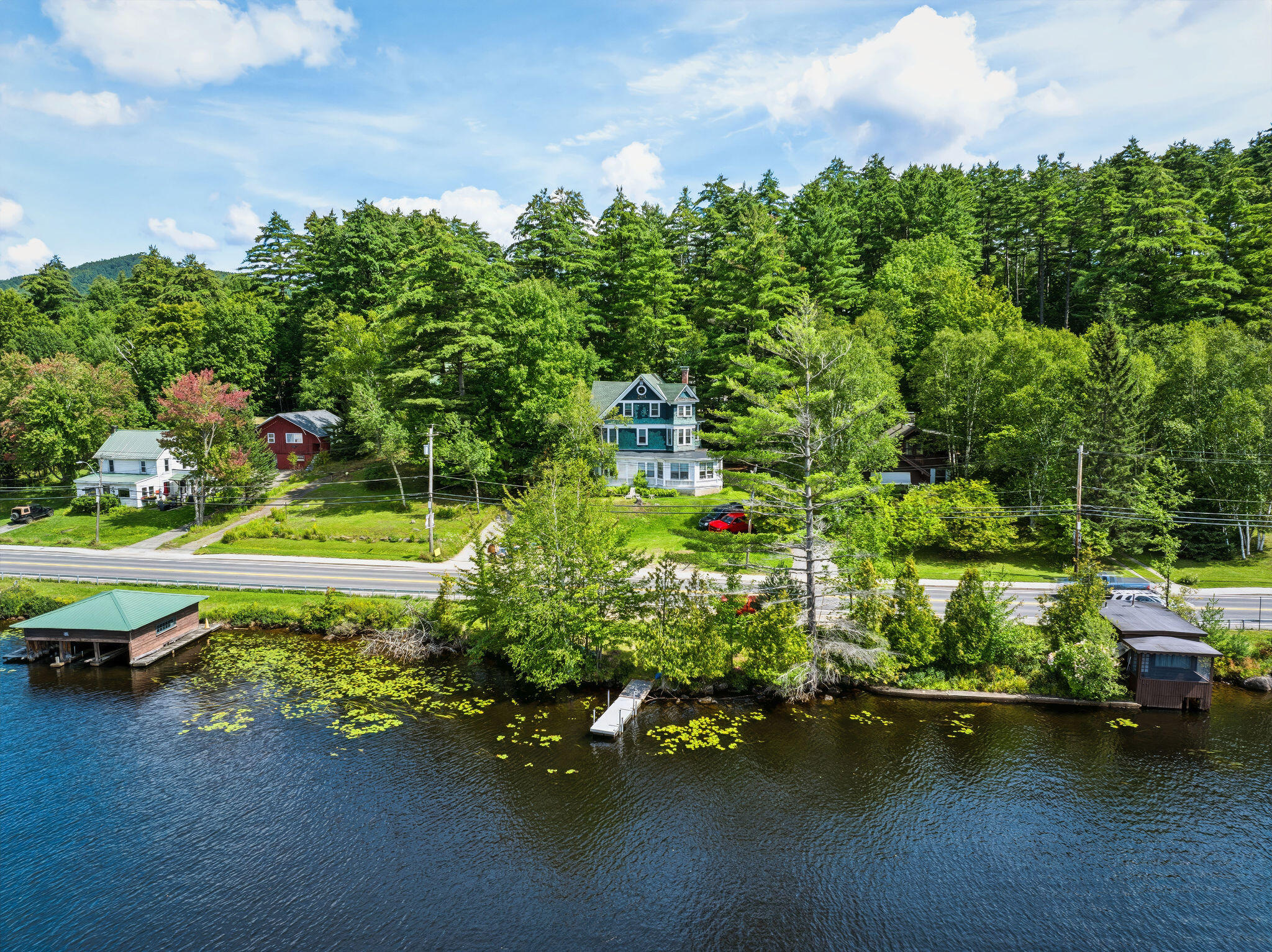 Waterfront house among trees, viewed across the lake with a dock and boathouses.