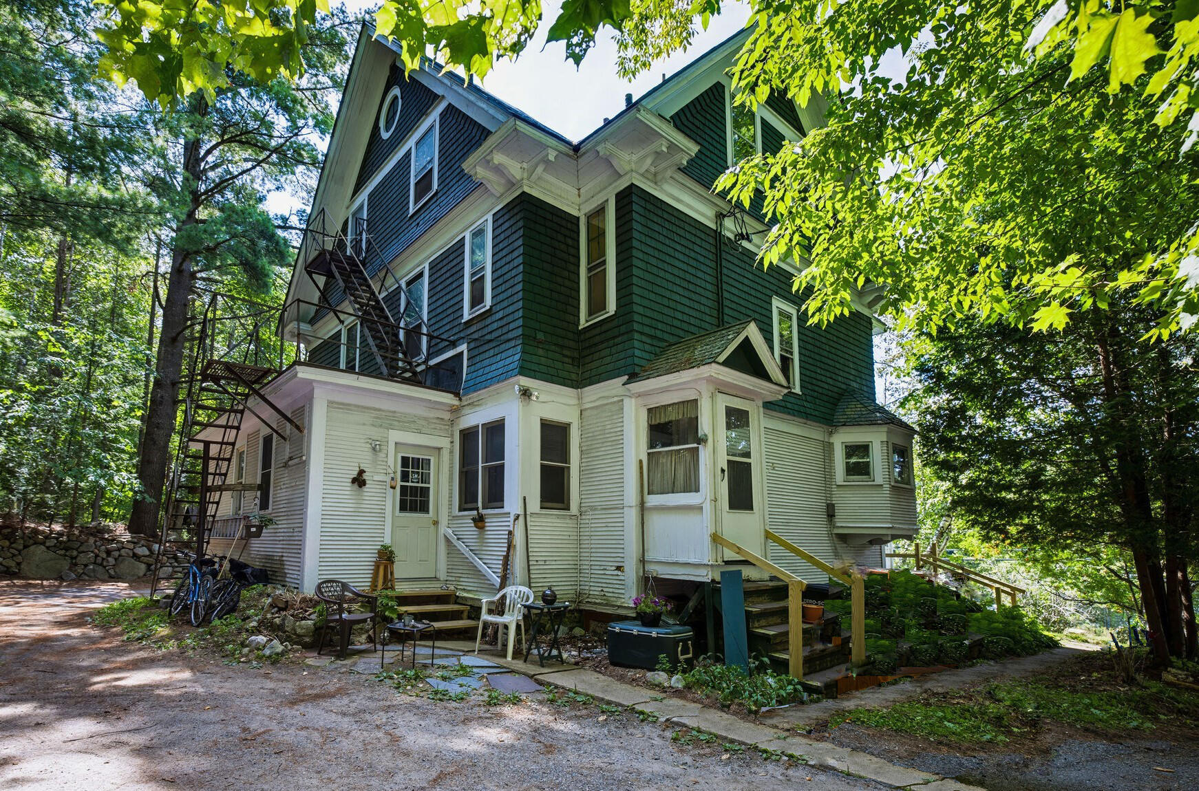 Multi-story green-and-white house among mature trees, with a metal exterior staircase and fire escape.