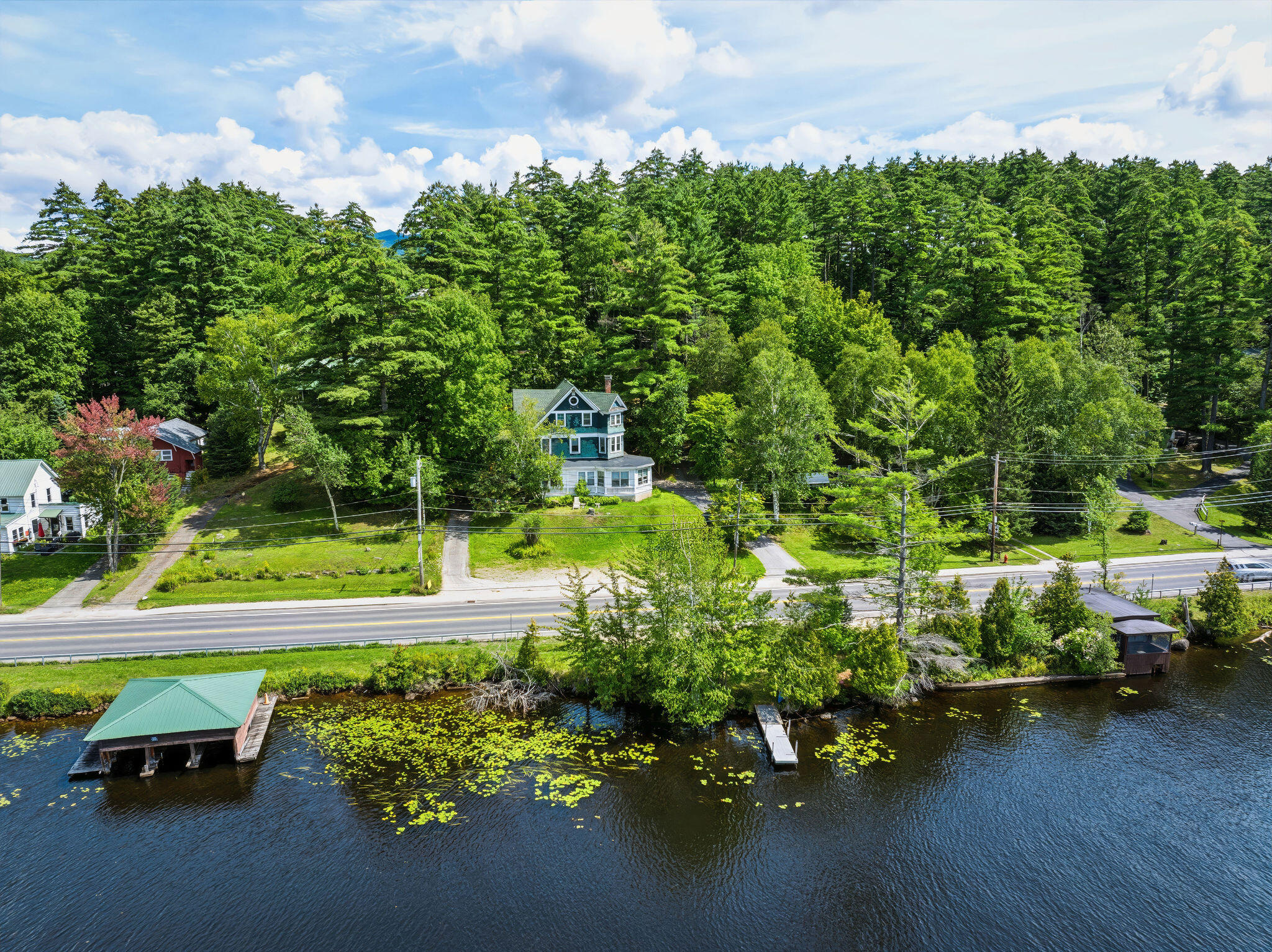 Aerial view of a lakeside home across the road from the water, with a boathouse and dock.