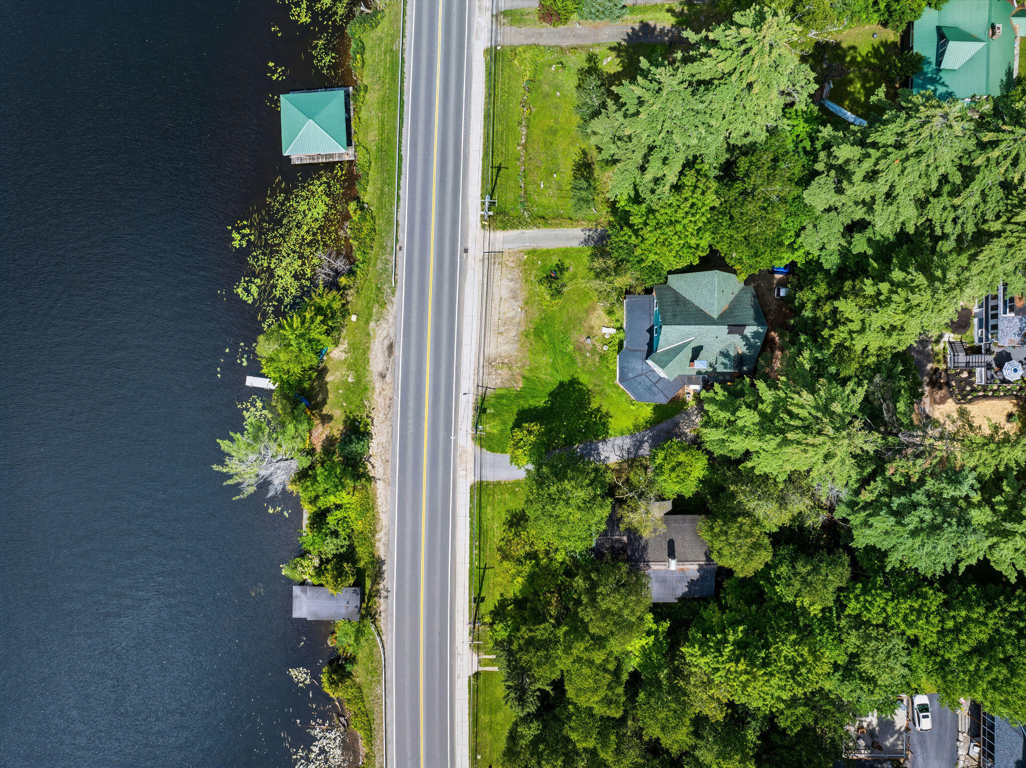 Aerial view of a wooded lakeside home with a dock and road along the shore.