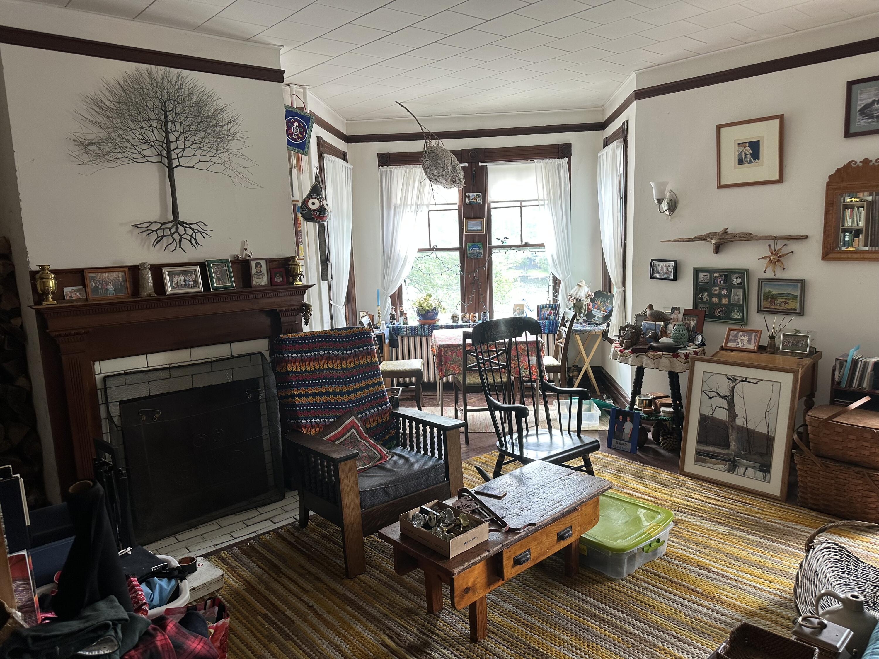 Living room with a dark wood fireplace, colorful rugs, eclectic furnishings, and large curtained windows.