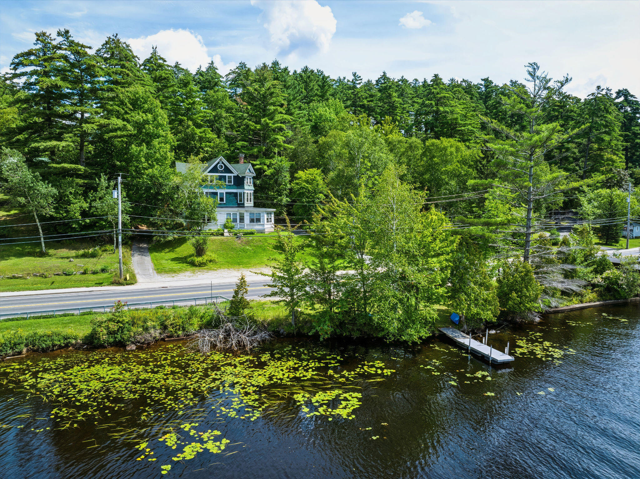 Teal-and-white house across a lily-pad-covered waterfront, with a small dock in the foreground.