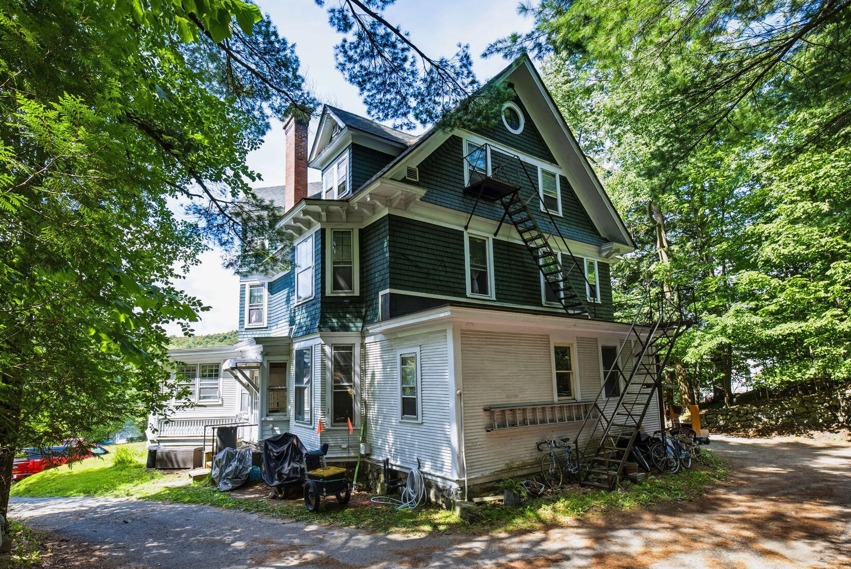 Multi-story shingle-sided house framed by trees, with a steep gable and exterior fire-escape stairs.