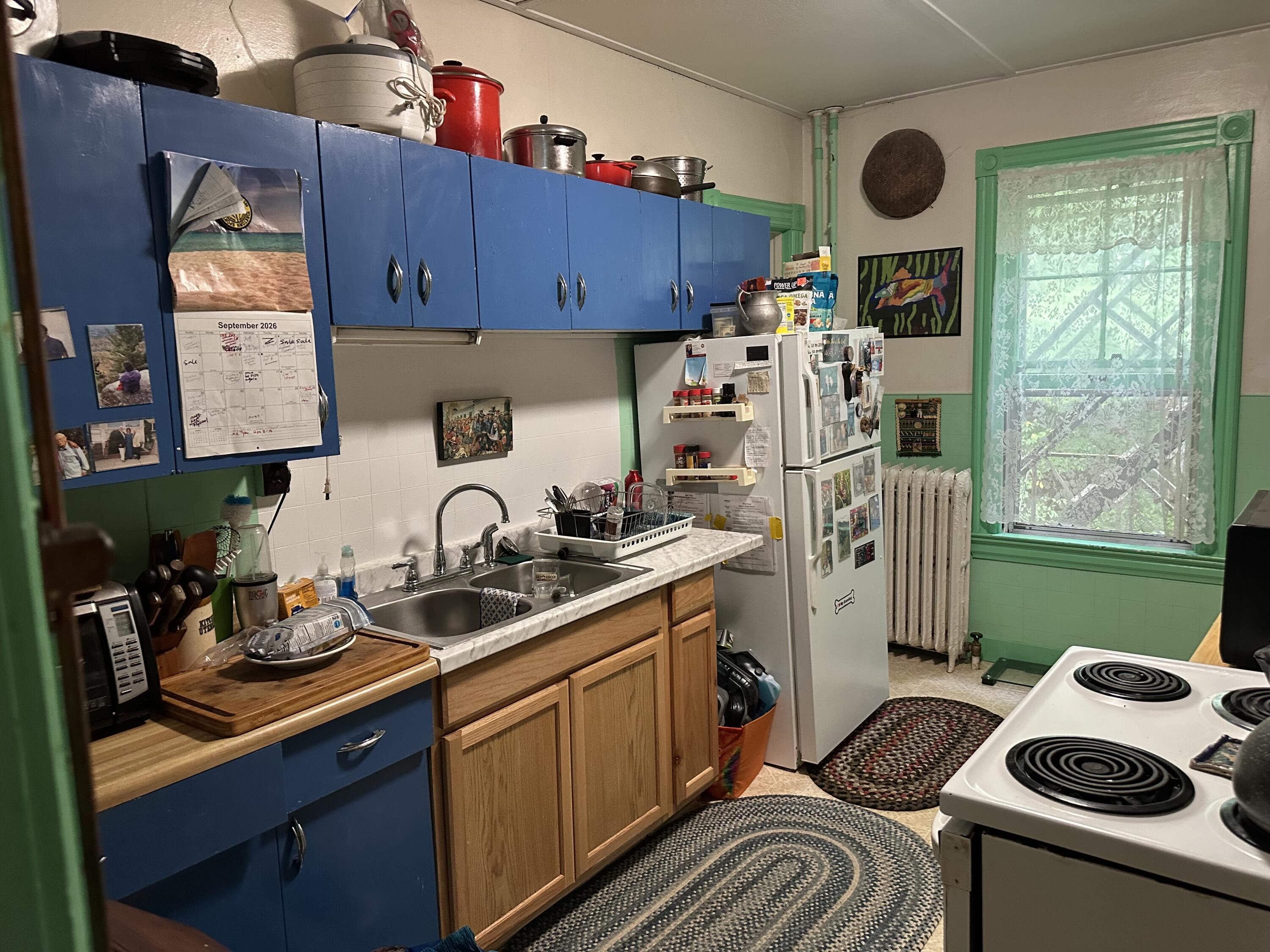 Kitchen with blue cabinets, wood counters, green window trim, and a lace curtain.