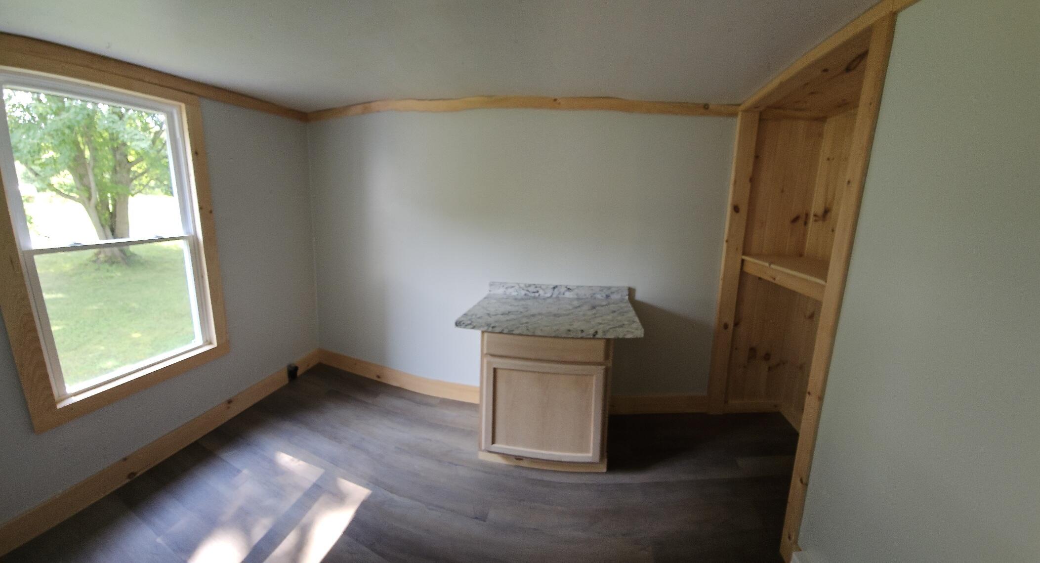 Empty room with gray plank flooring, wood trim, a large window, and a built-in wooden cupboard.