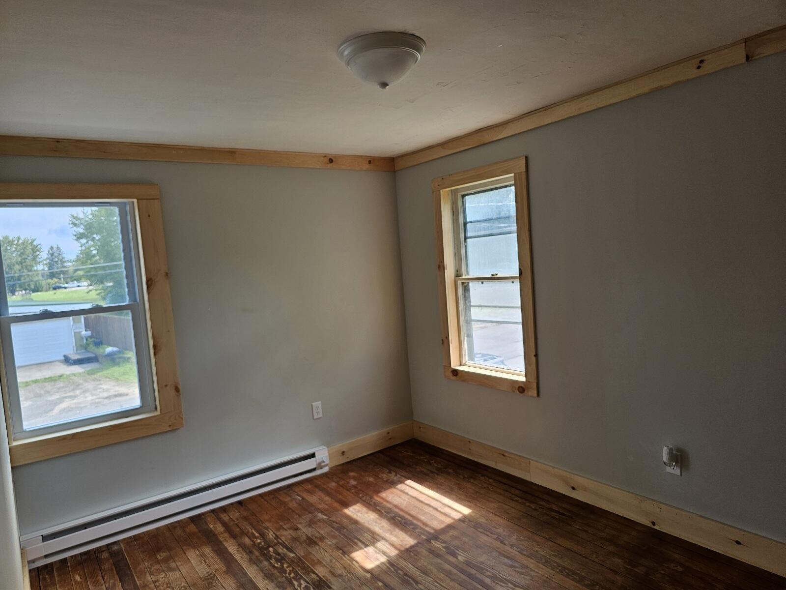 Empty room with wood-trimmed windows, gray walls, and worn hardwood floors.