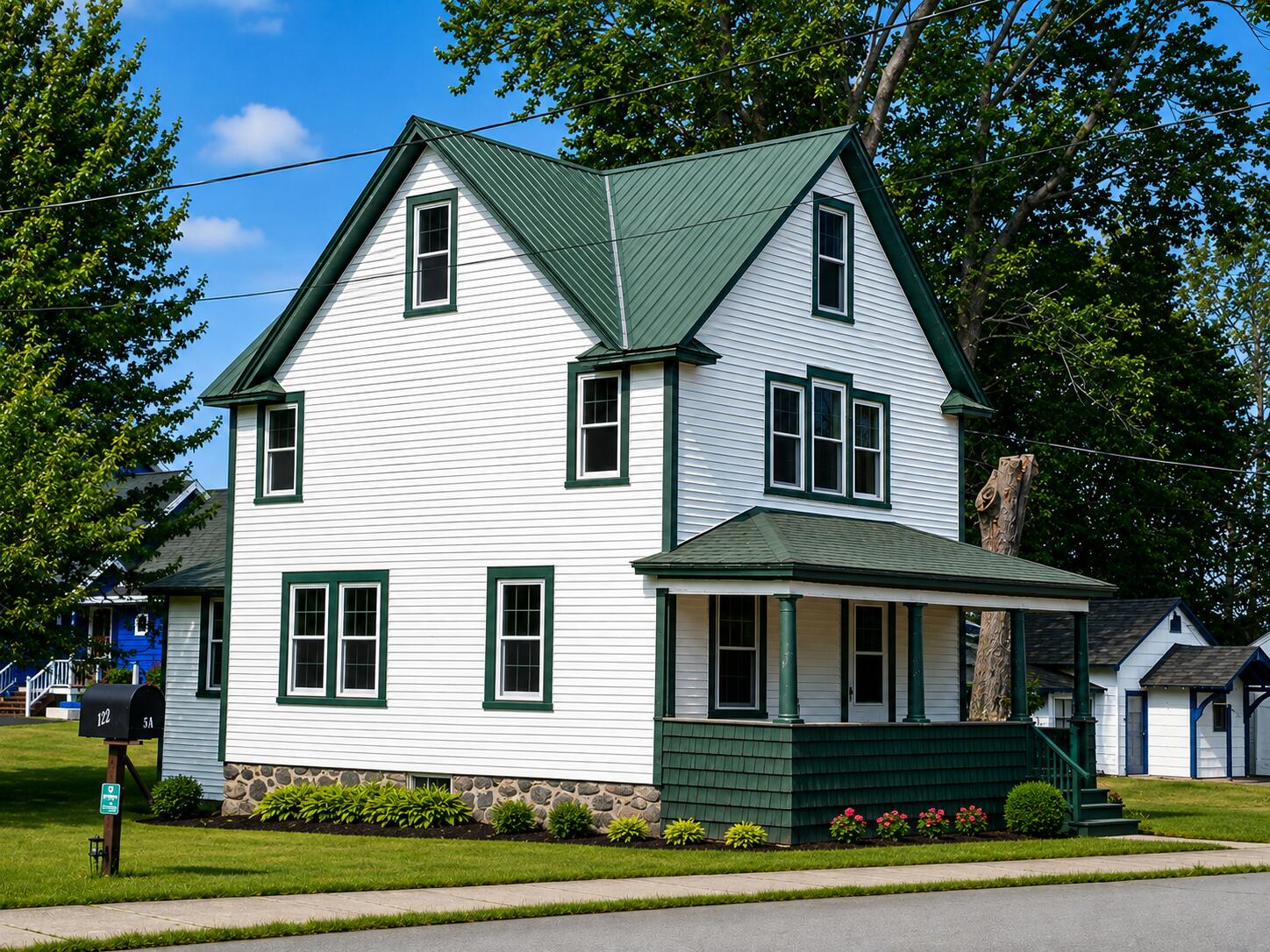 White two-story house with a steep green metal roof, covered porch, and stone foundation.