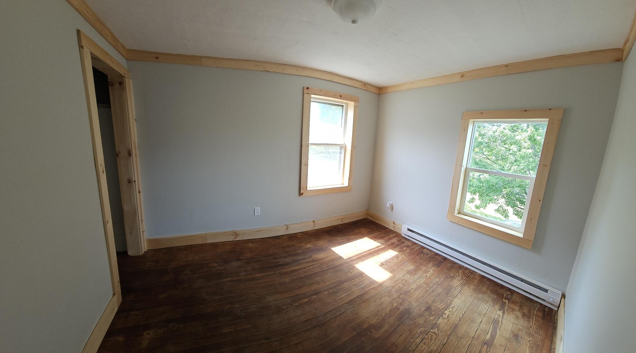 Empty room with dark hardwood floors, natural wood trim, and two windows.