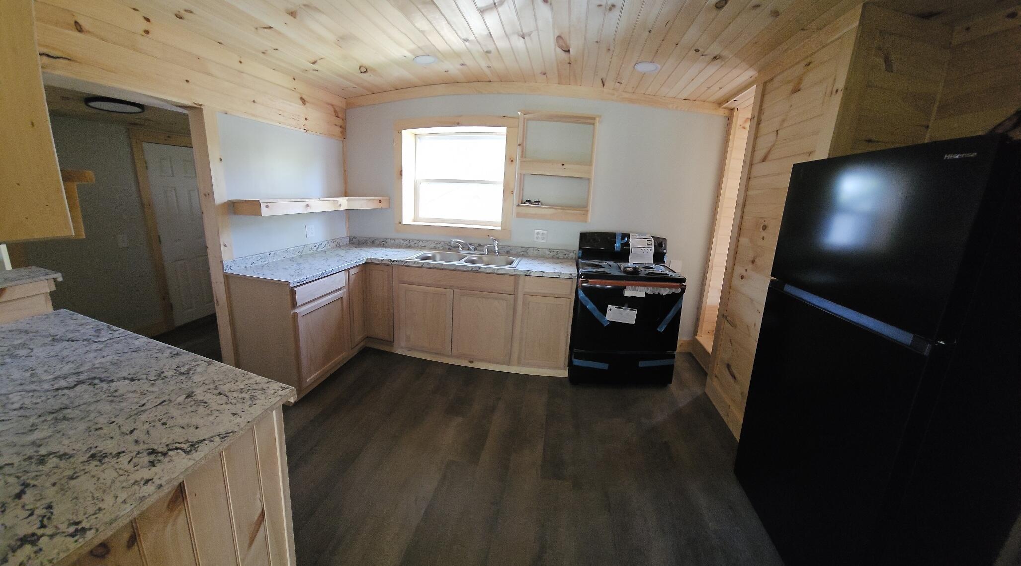 Kitchen with a vaulted wood-plank ceiling, stone counters, double sink, and black appliances.