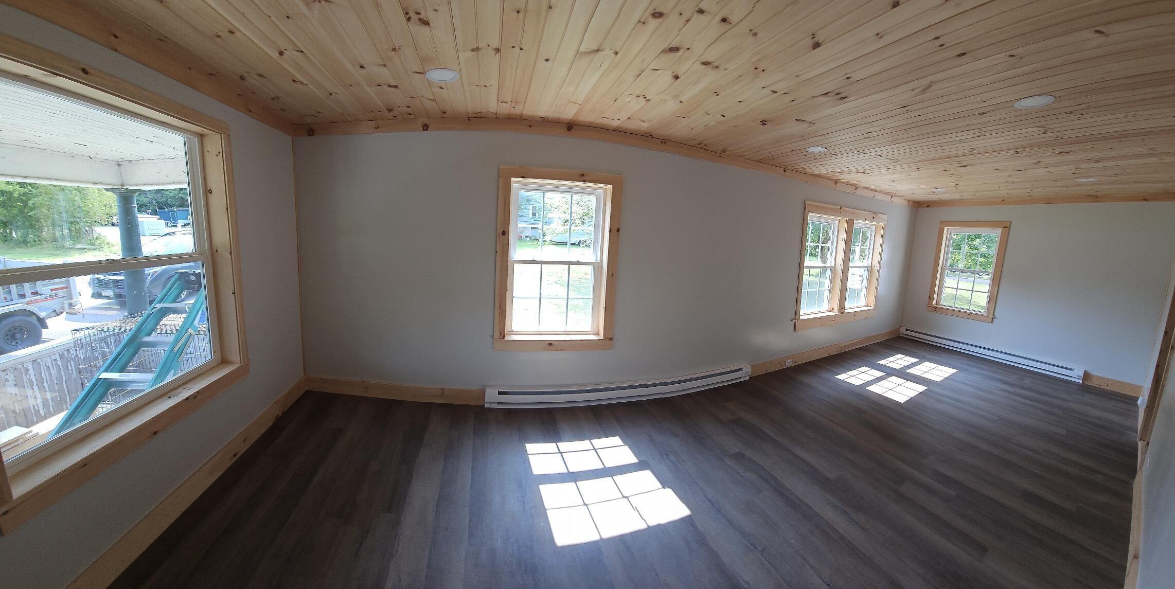 Vacant room with a vaulted pine ceiling, dark plank flooring, and sunlight streaming through several windows.