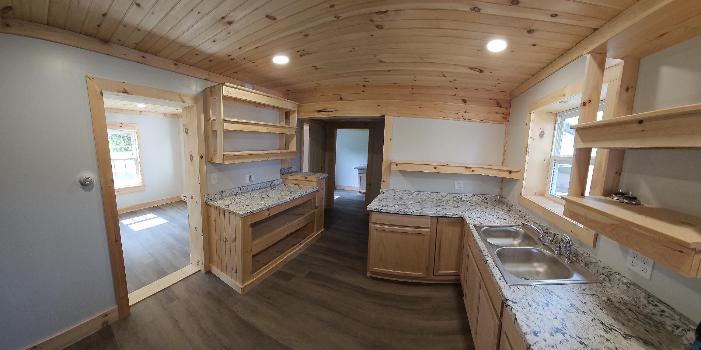 Kitchen with granite counters, a double sink, custom wood shelving, and a knotty pine ceiling.