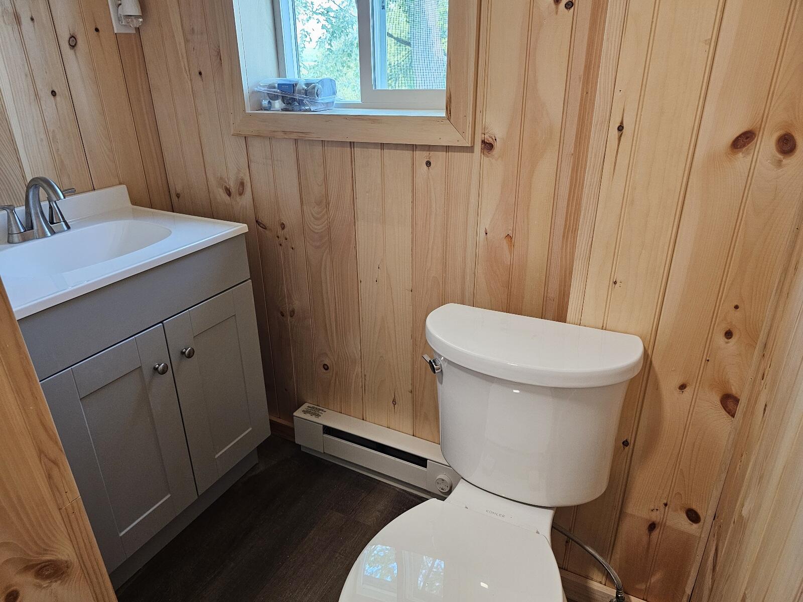 Bathroom with knotty pine walls, white vanity and toilet, and a window.