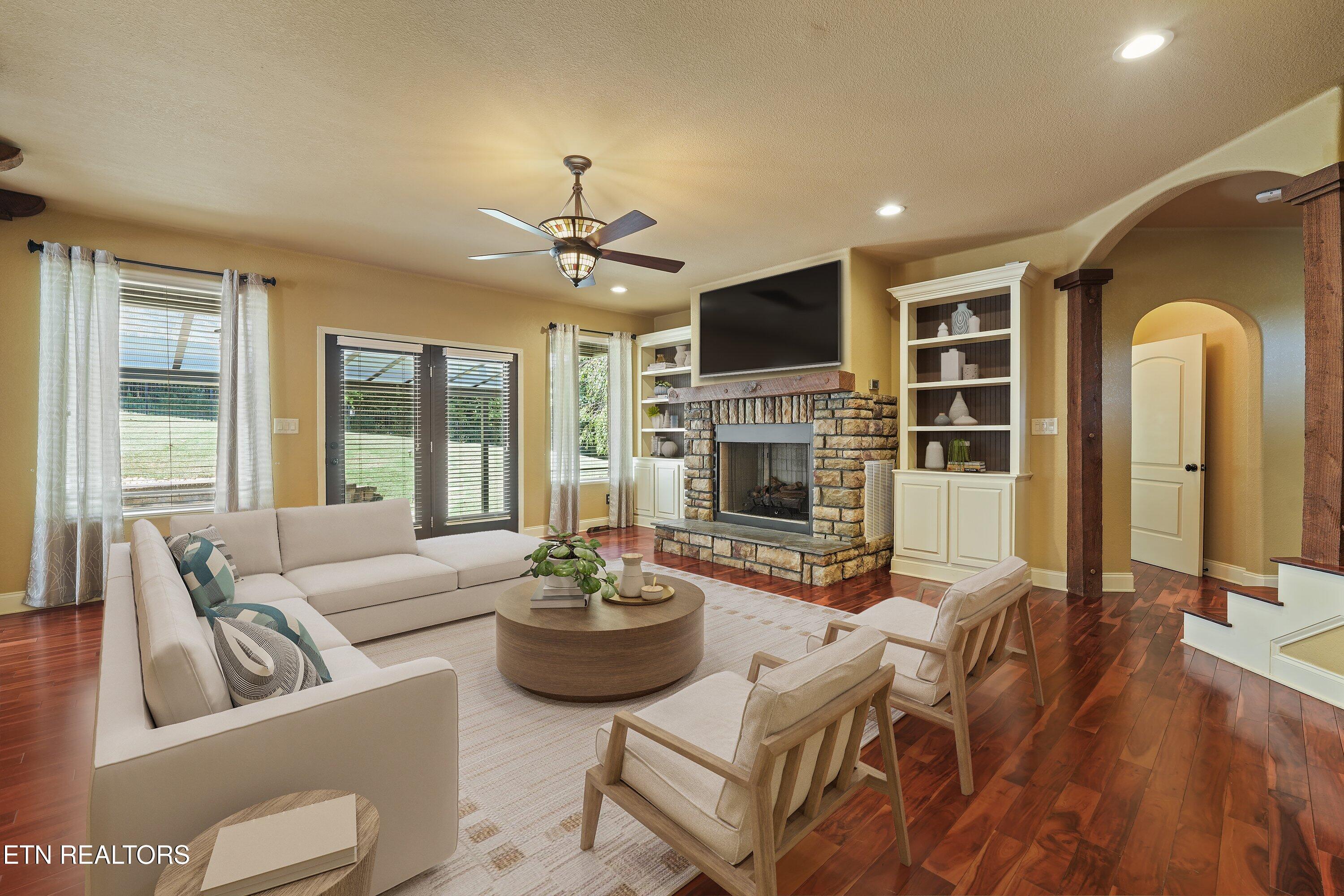 Living room with a stone fireplace, built-in shelving, cream seating, and dark hardwood floors.