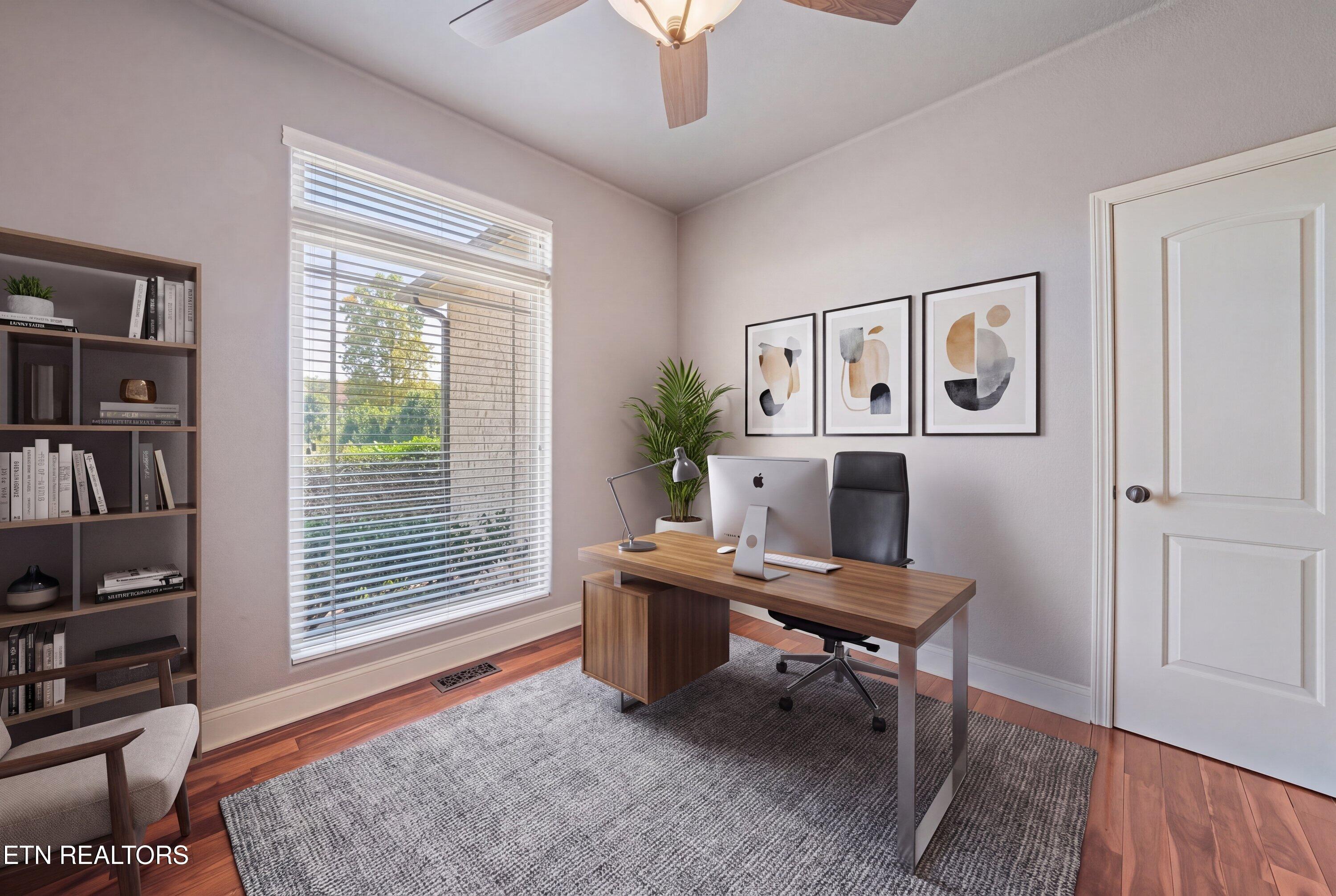 Furnished home office with a wood desk and computer beside a large window with blinds.