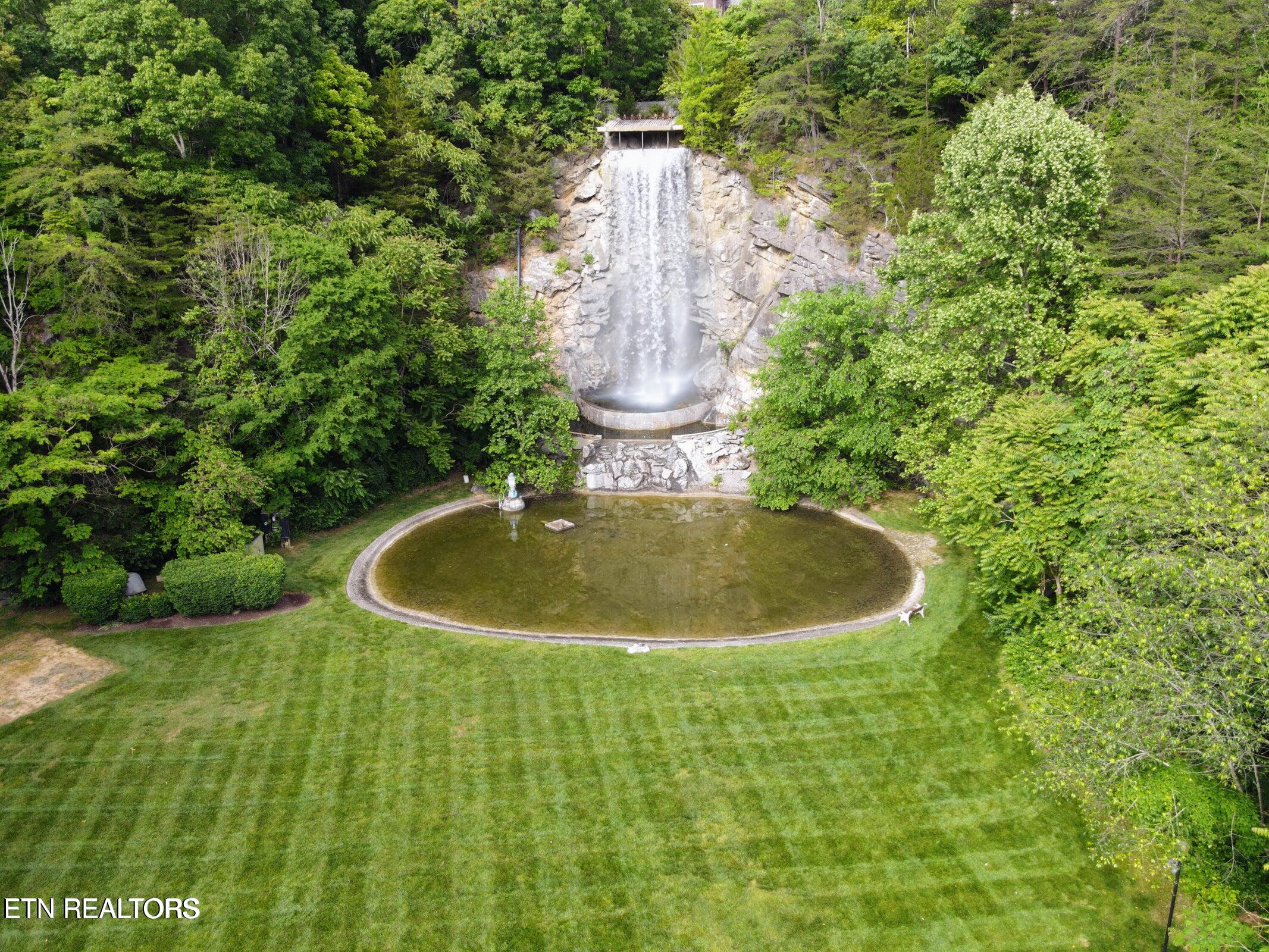 Aerial view of a landscaped lawn with a large rock waterfall flowing into a round pond.