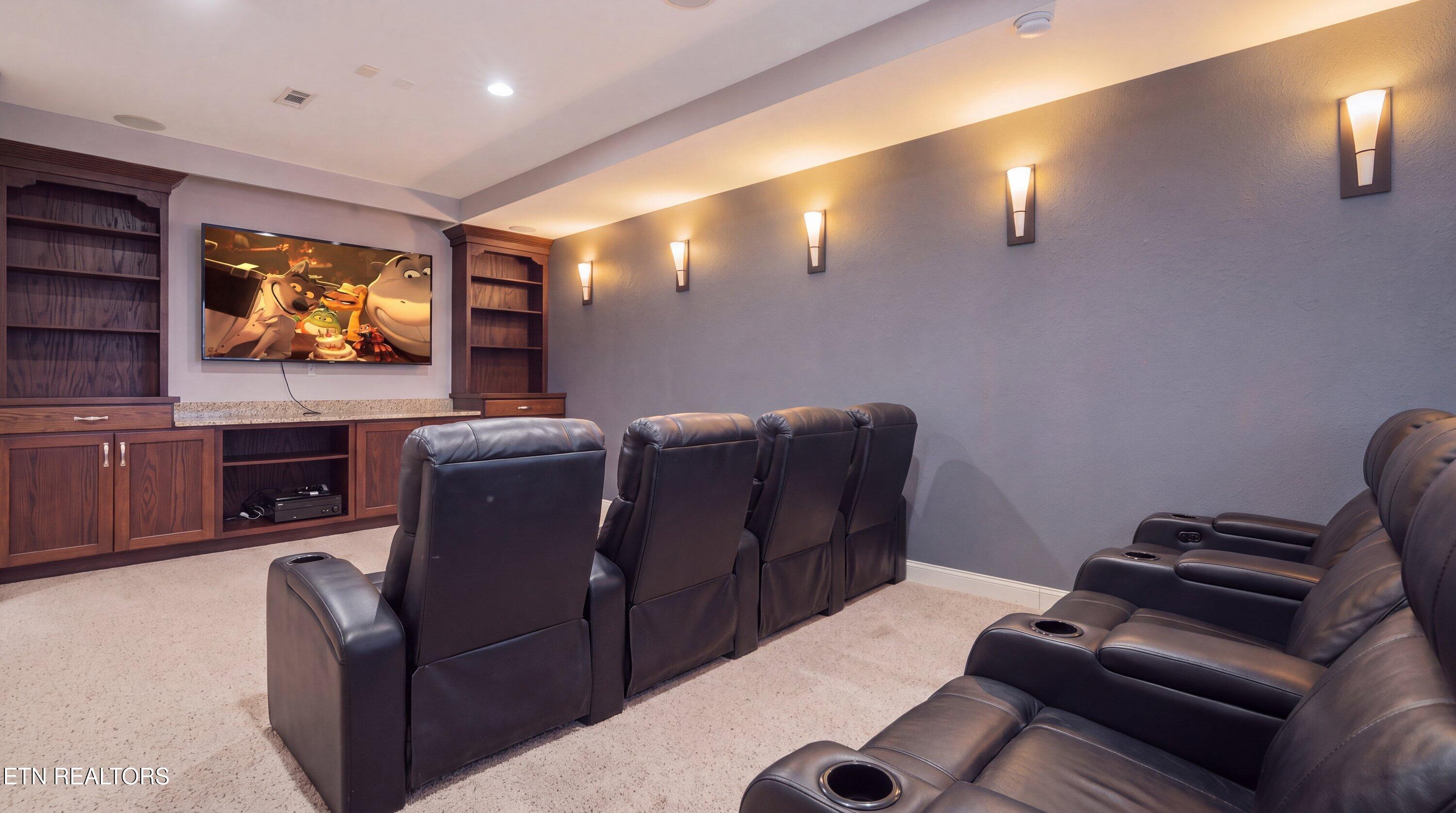 Furnished home theater with leather recliners, built-in wood cabinetry, and warm wall sconces.
