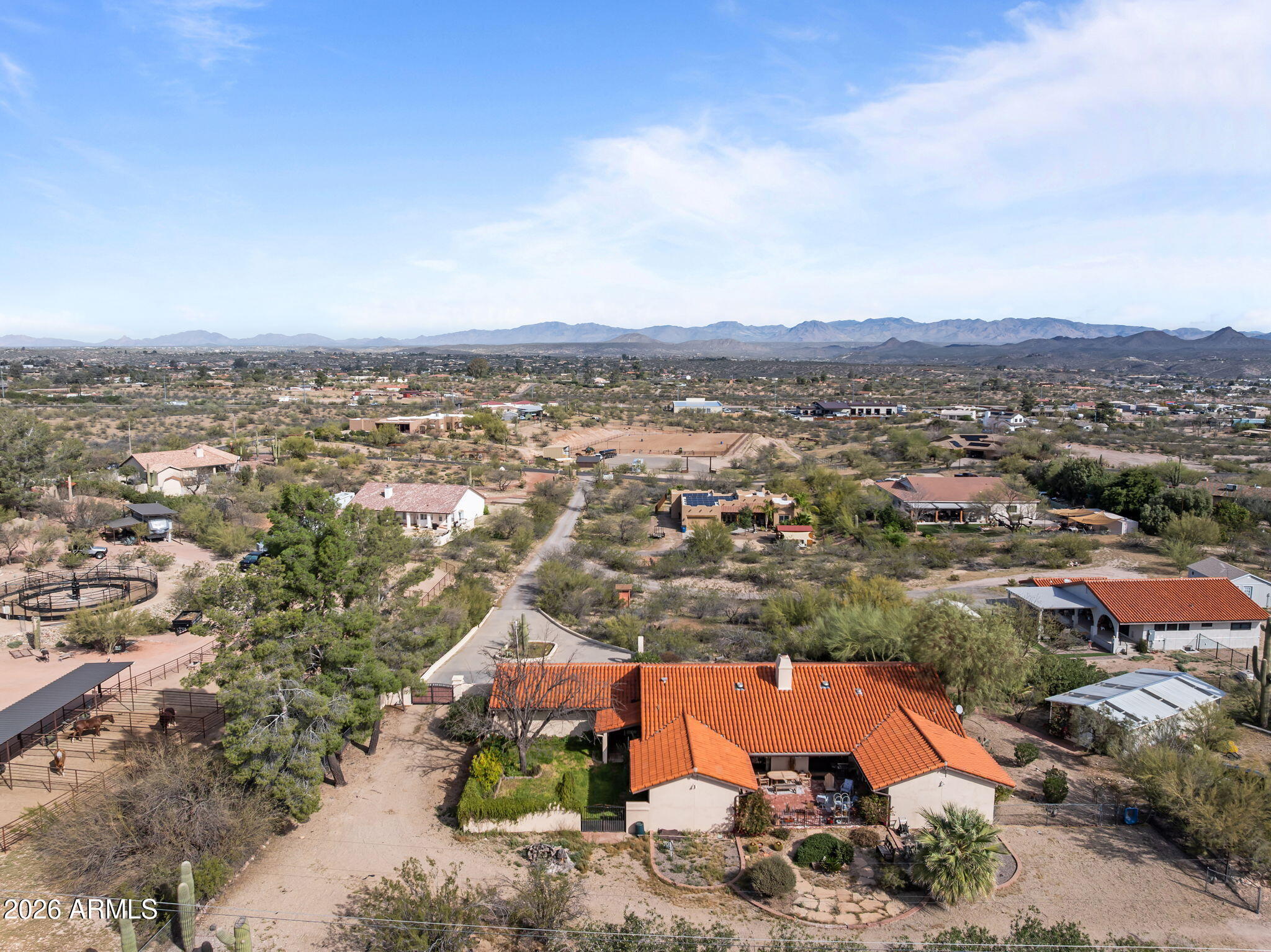 Aerial view of a red-tile-roof home among desert properties, with mountains in the distance.