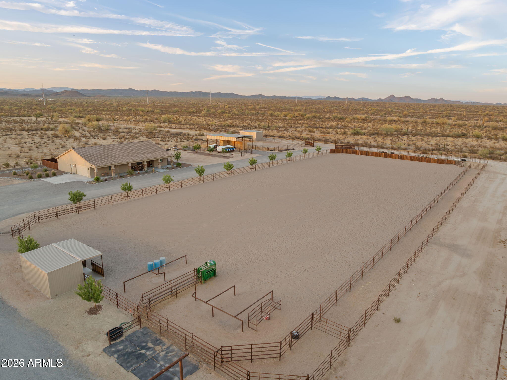 Aerial view of a desert horse property with a large fenced arena and mountains in the distance.