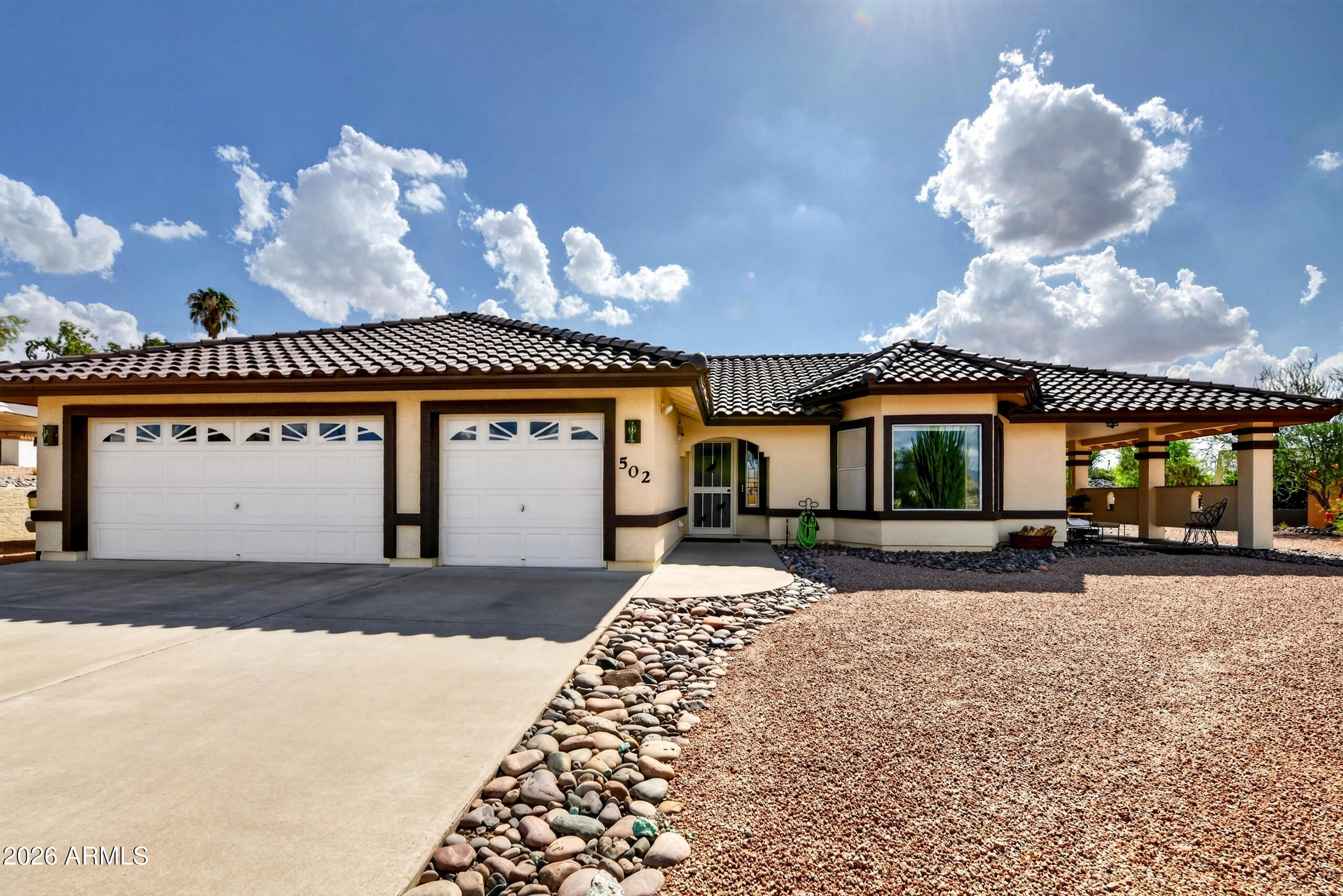 Single-story stucco home with two garage doors, a tiled roof, and a covered patio.