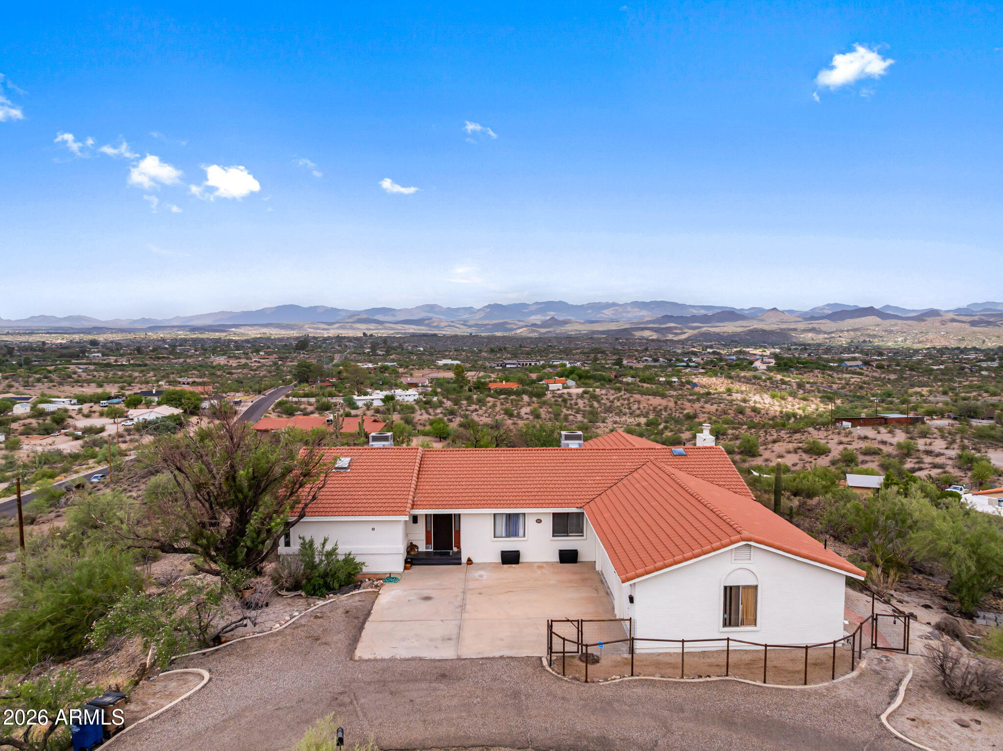 Single-story stucco home with a terracotta tile roof overlooking desert terrain and distant mountains.