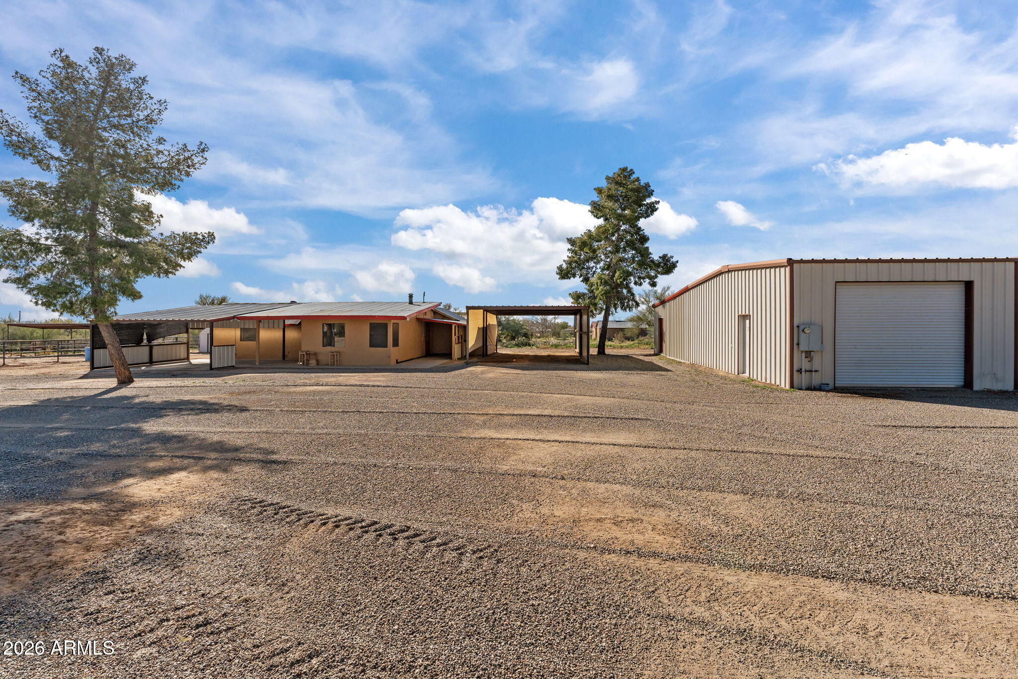 Rural property with a single-story home, covered carport, detached metal garage, and broad gravel yard.