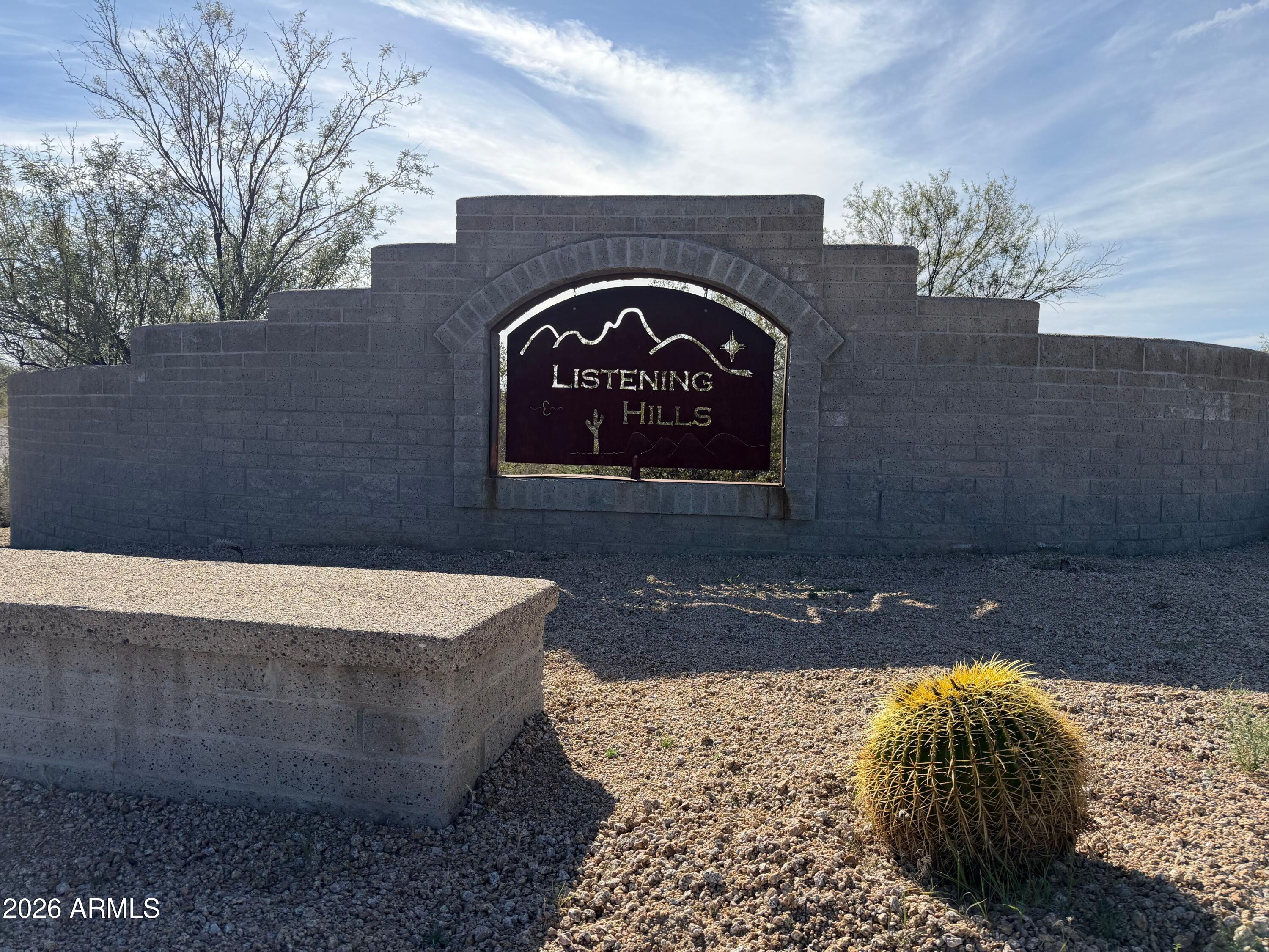 Listening Hills neighborhood entrance sign set in a gray block wall amid desert landscaping.