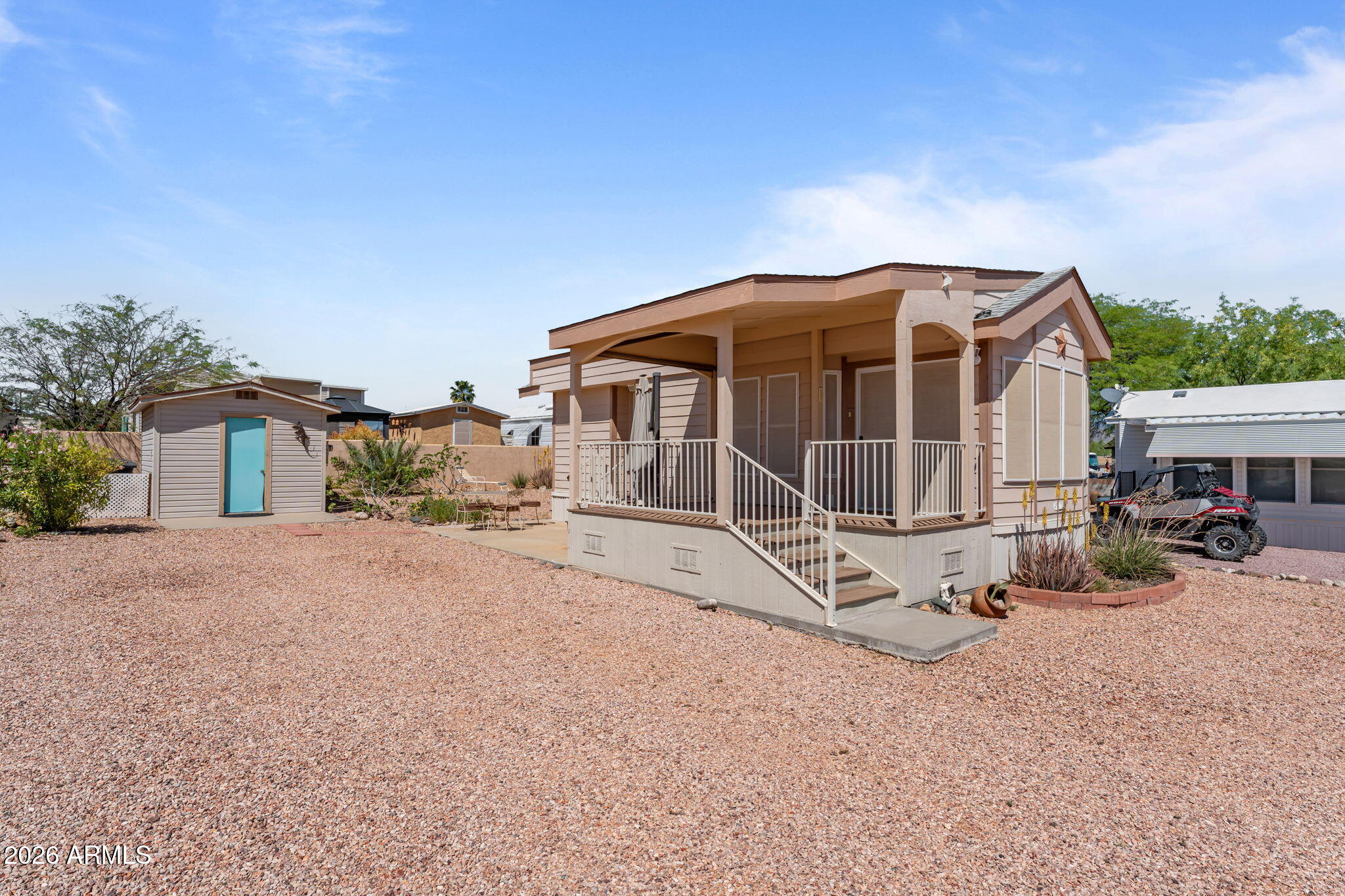 Small home with a covered porch and gravel yard, beside a shed with a turquoise door.