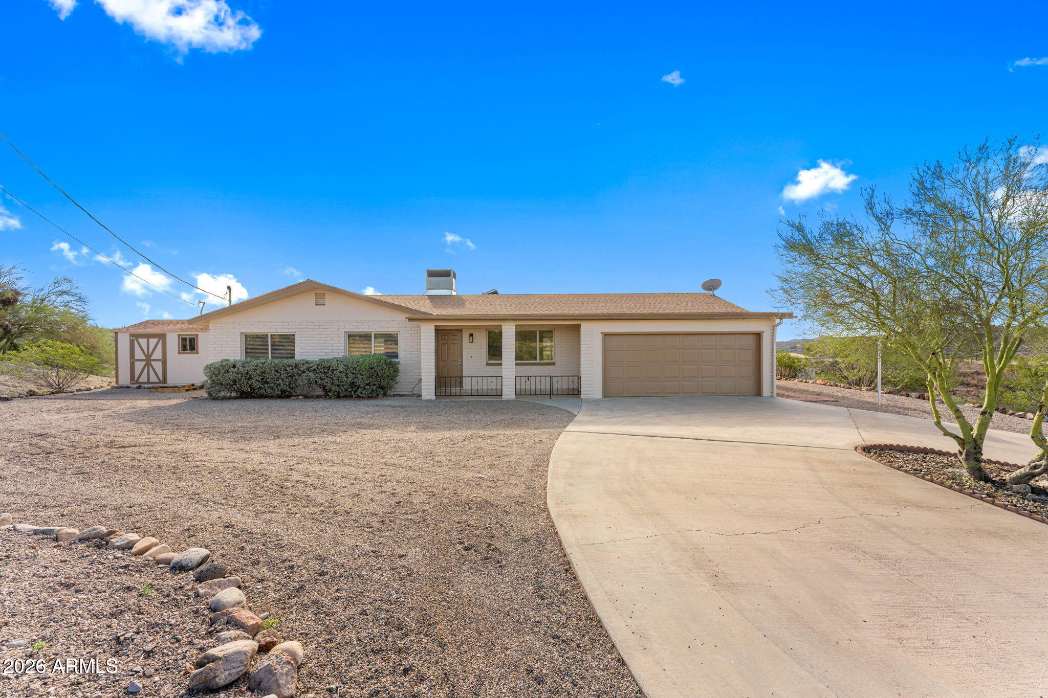 Single-story home with a two-car garage, gravel landscaping, and a curved driveway.