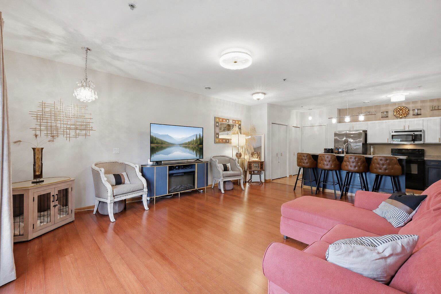 Open-plan living room with a pink sectional, white accent chairs, and kitchen breakfast bar.
