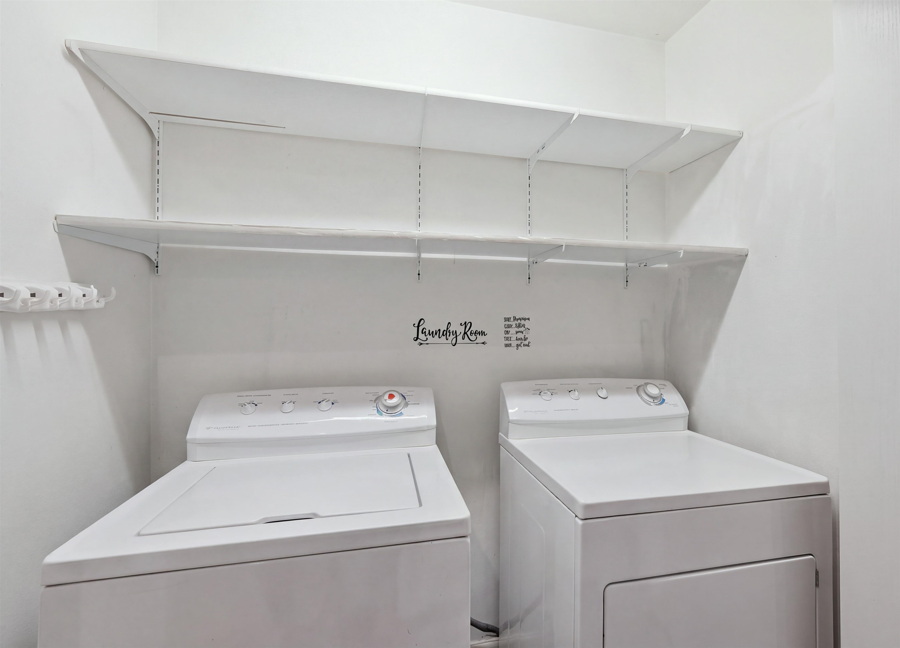 Laundry room with a white washer and dryer beneath long wall-mounted shelves.