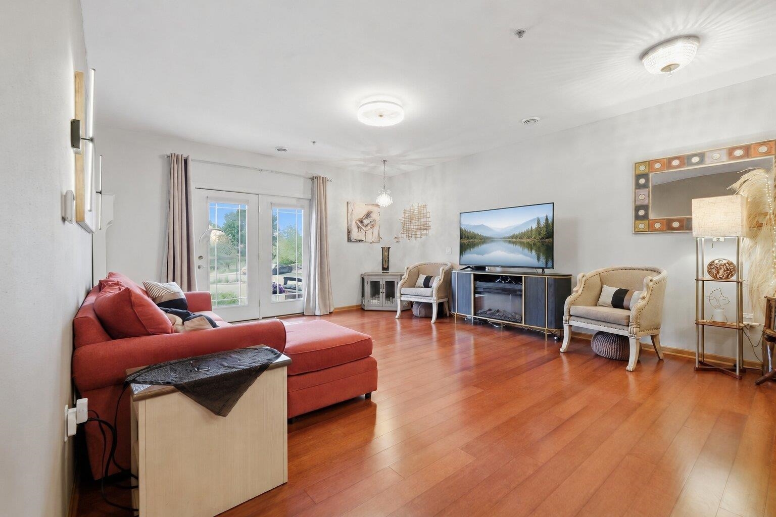 Living room with a red sectional, hardwood floors, and French doors opening to a patio.