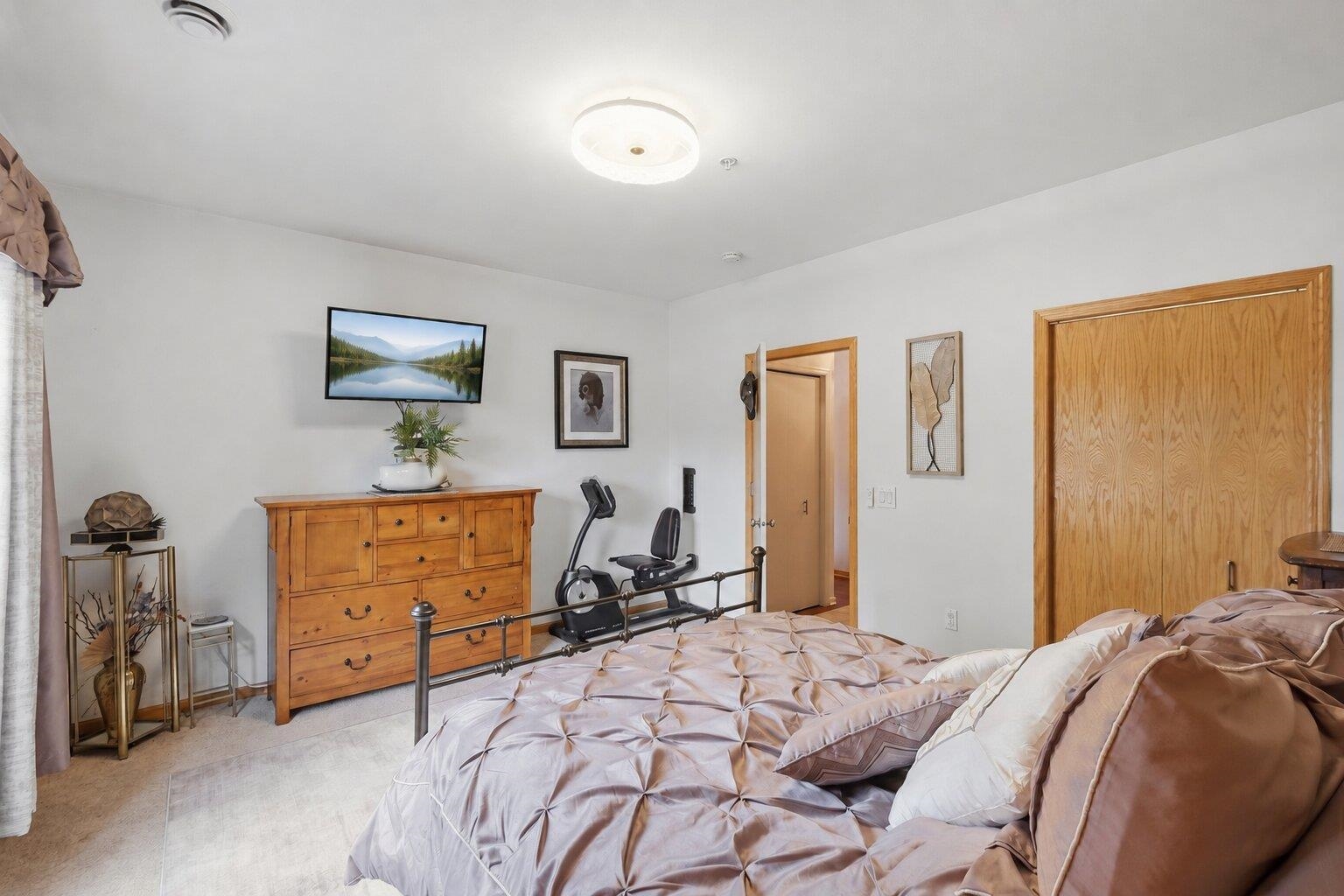Bedroom with a tufted blush bed, wooden dresser, and exercise bike.