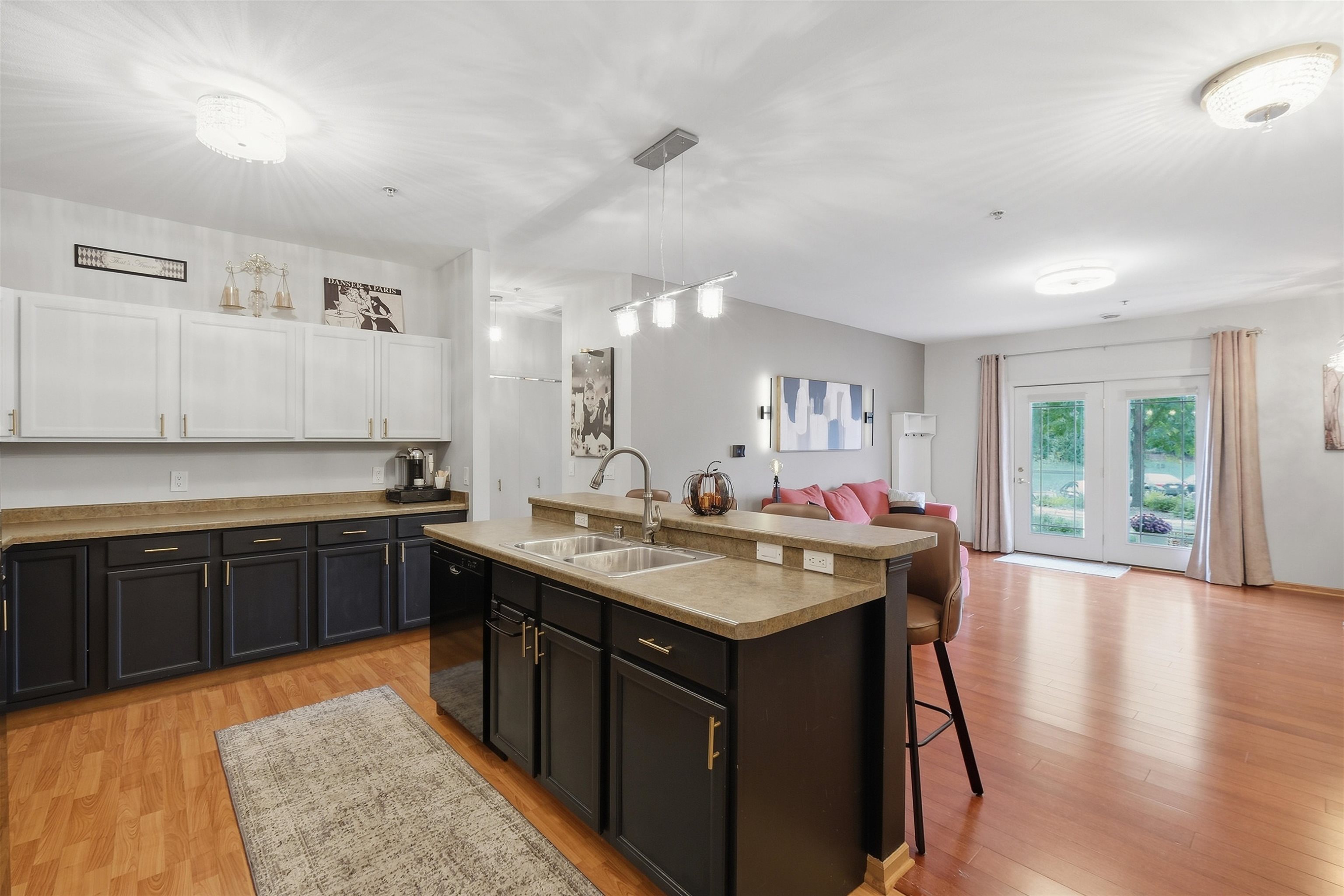 Open-plan kitchen with a large double-sink island and dark cabinetry, opening onto a living area with patio doors.
