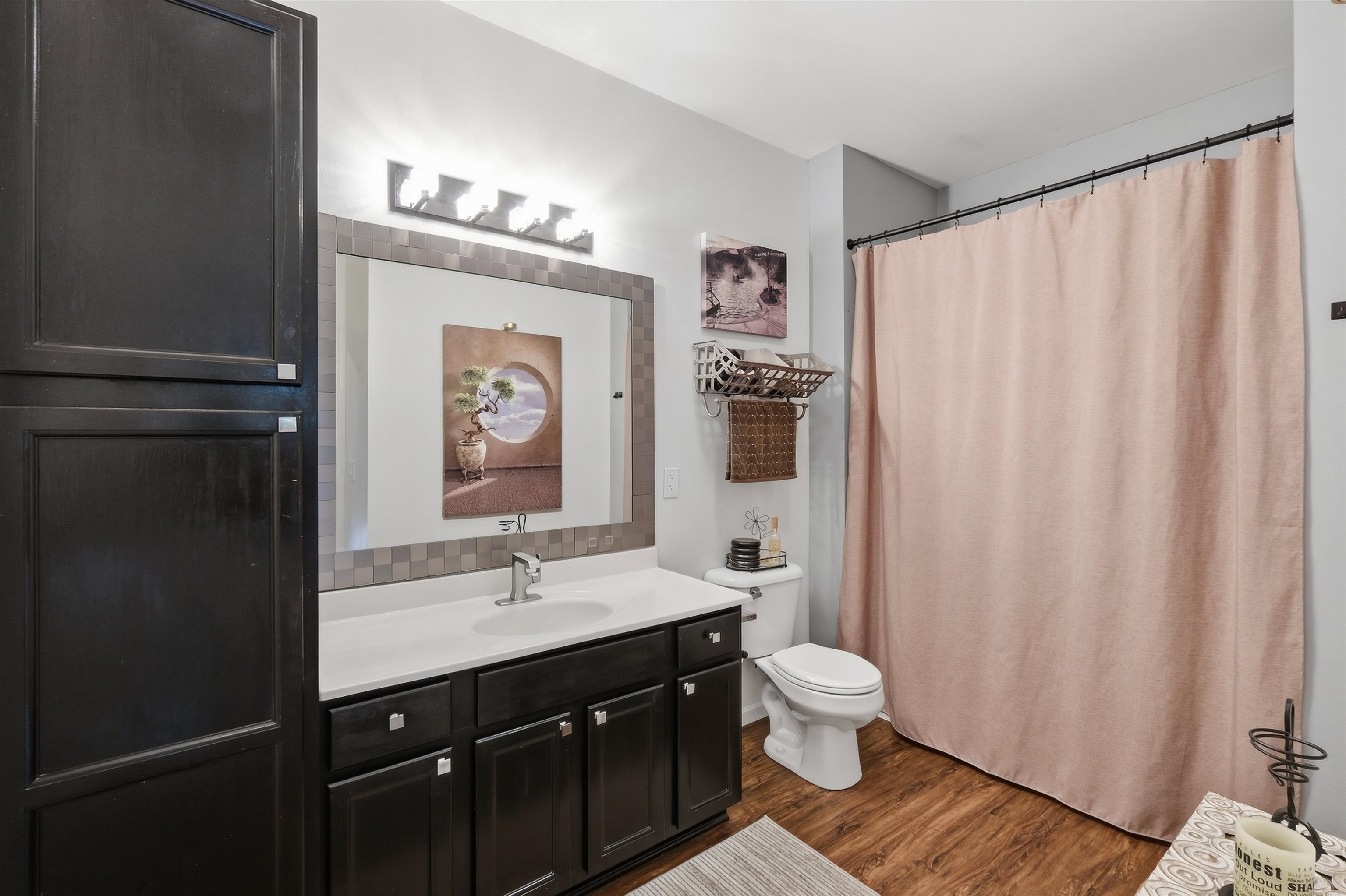 Bathroom with a dark wood vanity, tiled-framed mirror, toilet, and blush pink shower curtain.