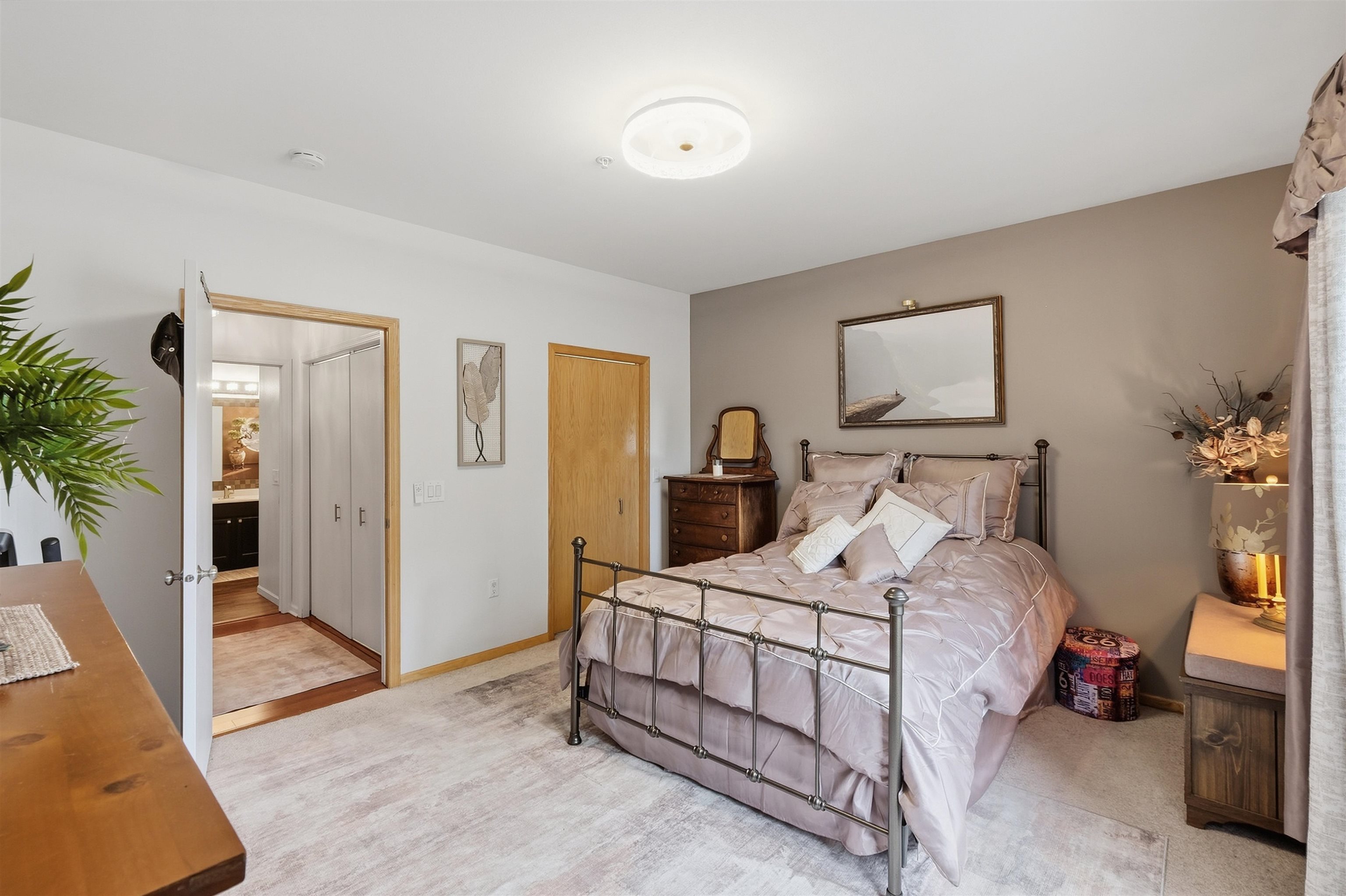 Furnished bedroom with a metal-frame bed, pale mauve bedding, and taupe accent wall.