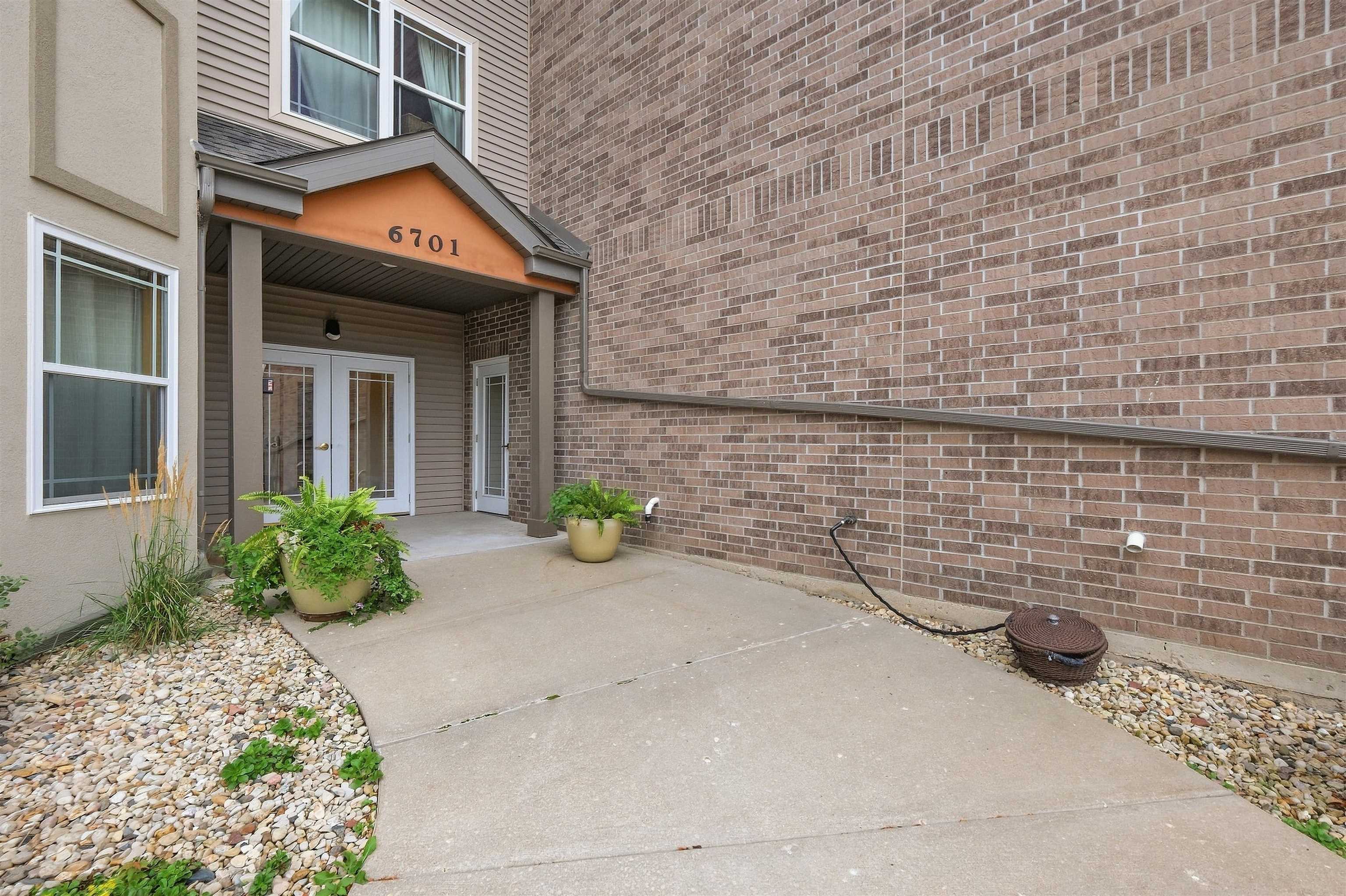Covered building entrance with glass double doors, brick wall, and potted ferns beside the walkway.