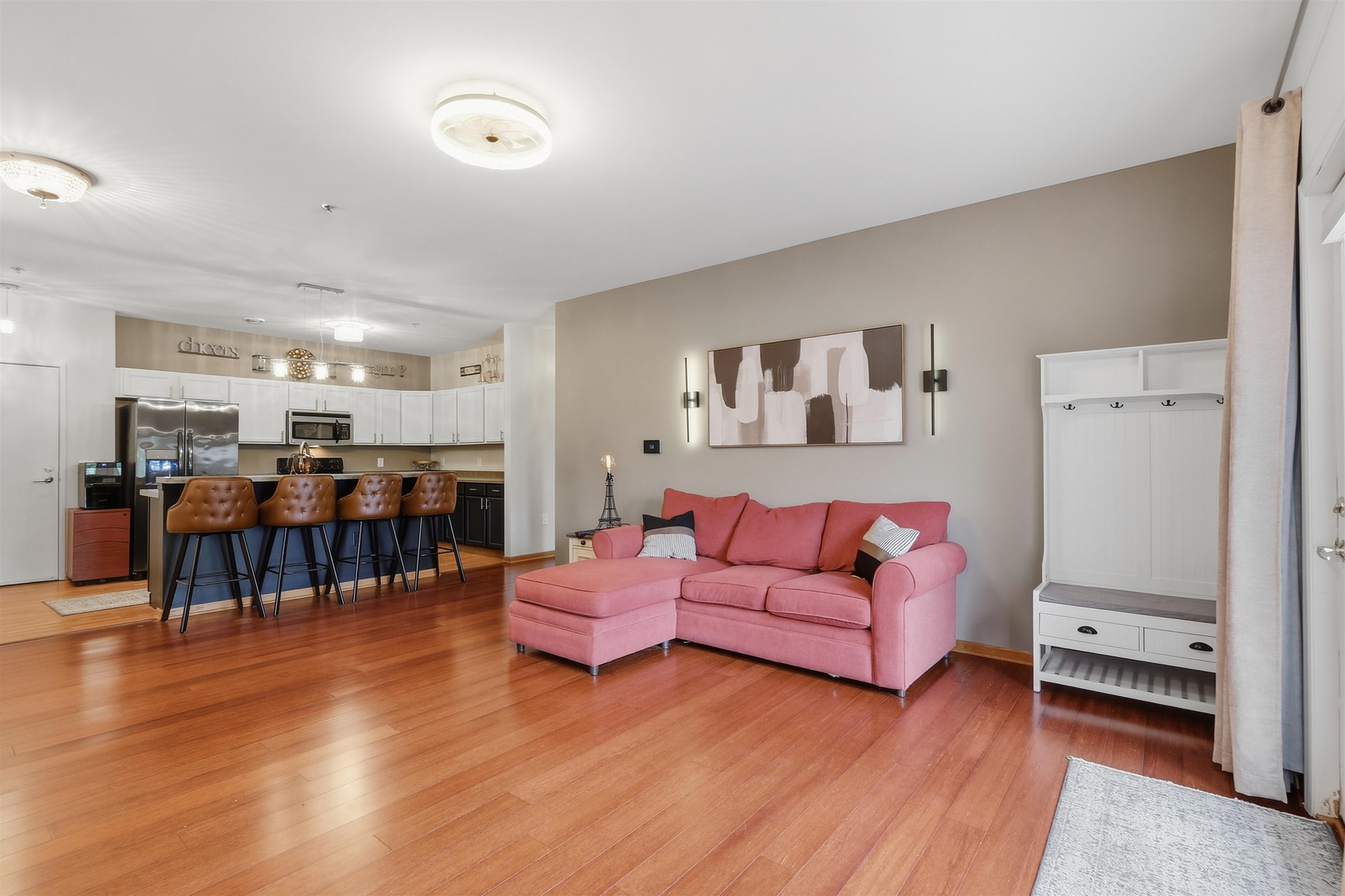 Open-plan living room and kitchen with a pink sectional, leather bar stools, and reddish hardwood floors.