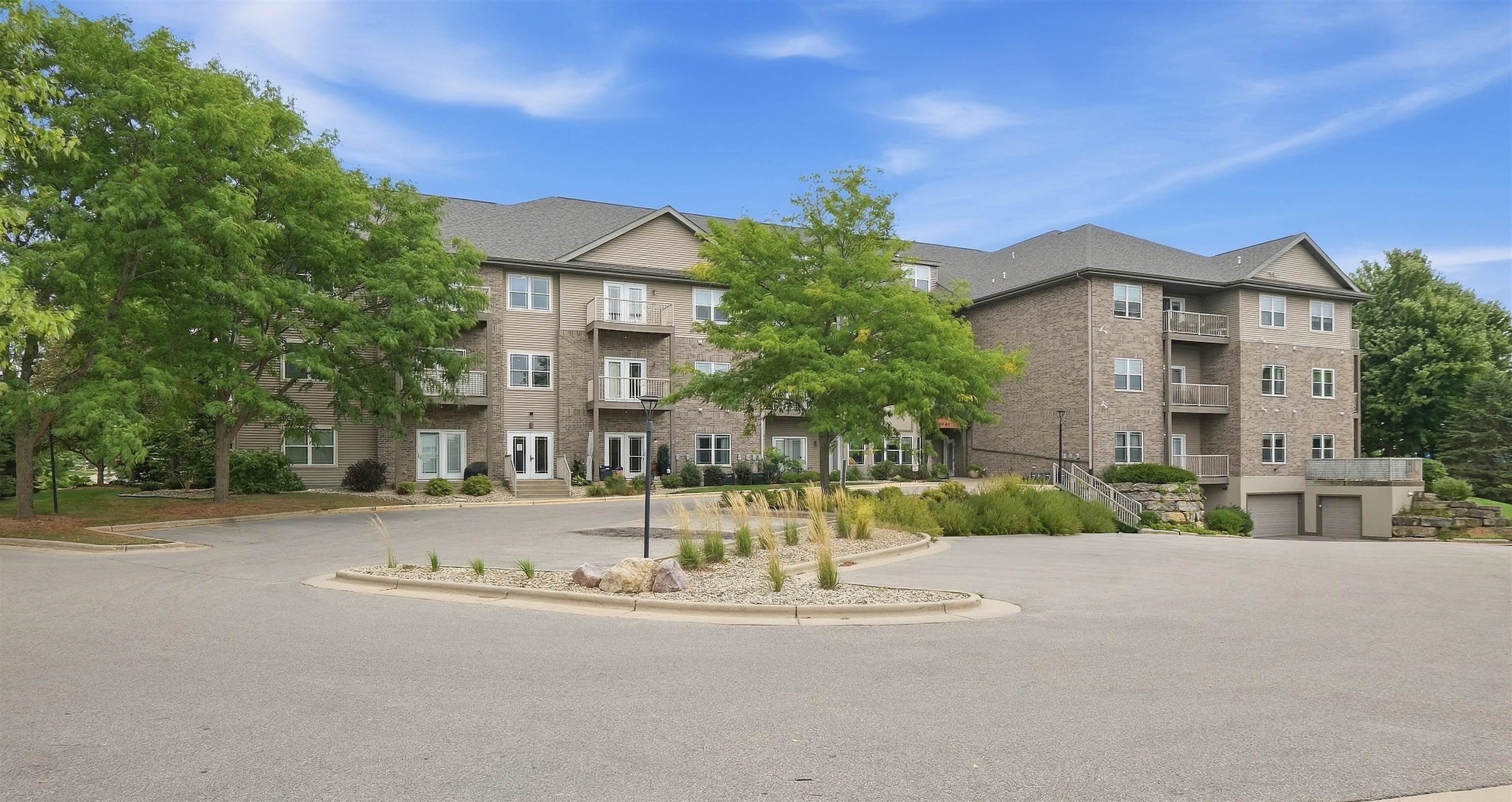 Multi-story condominium building with brick and beige siding, balconies, and landscaped grounds.