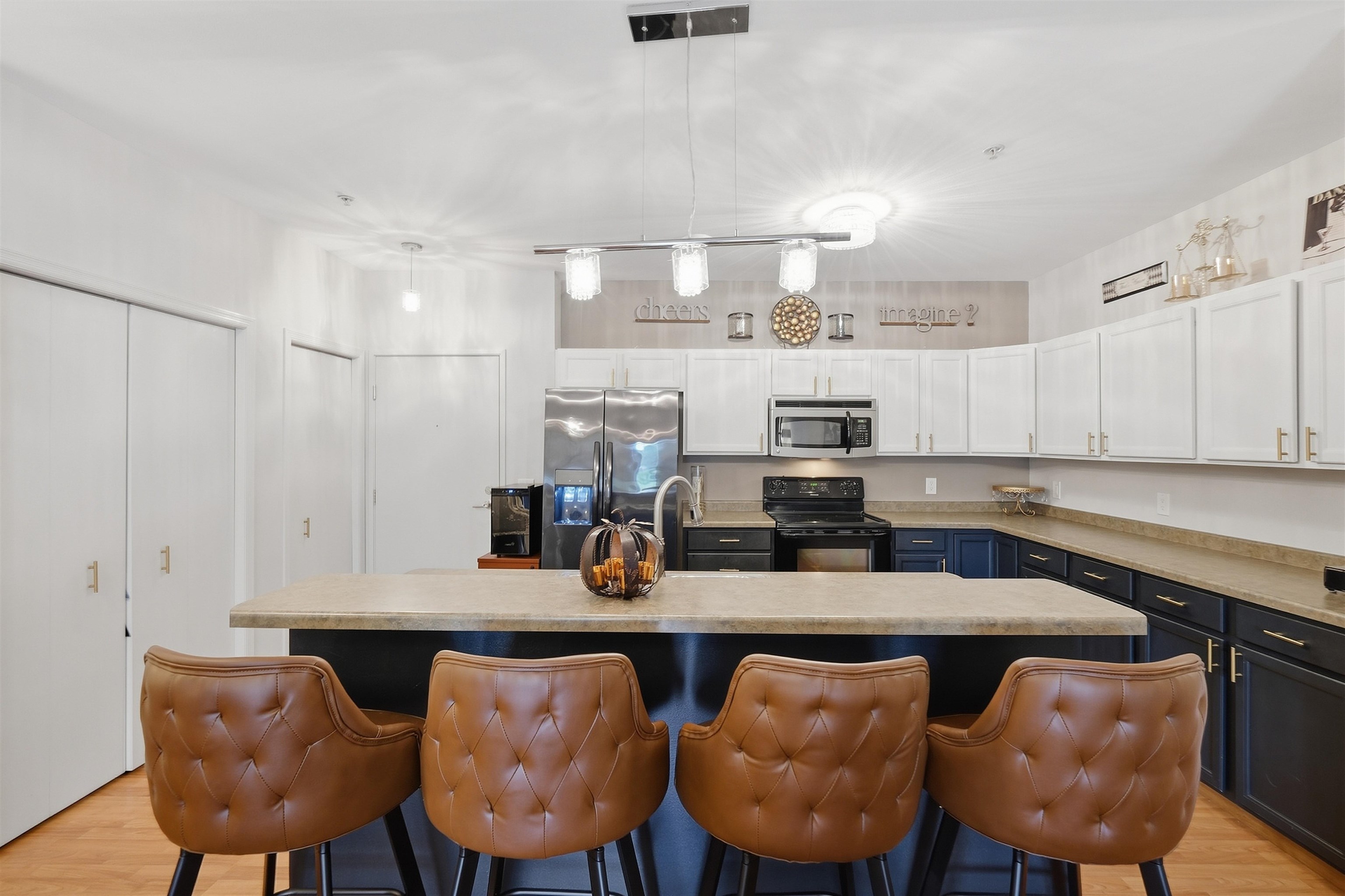 Kitchen with a stone-topped island, navy lower cabinets, and four brown leather bar stools.