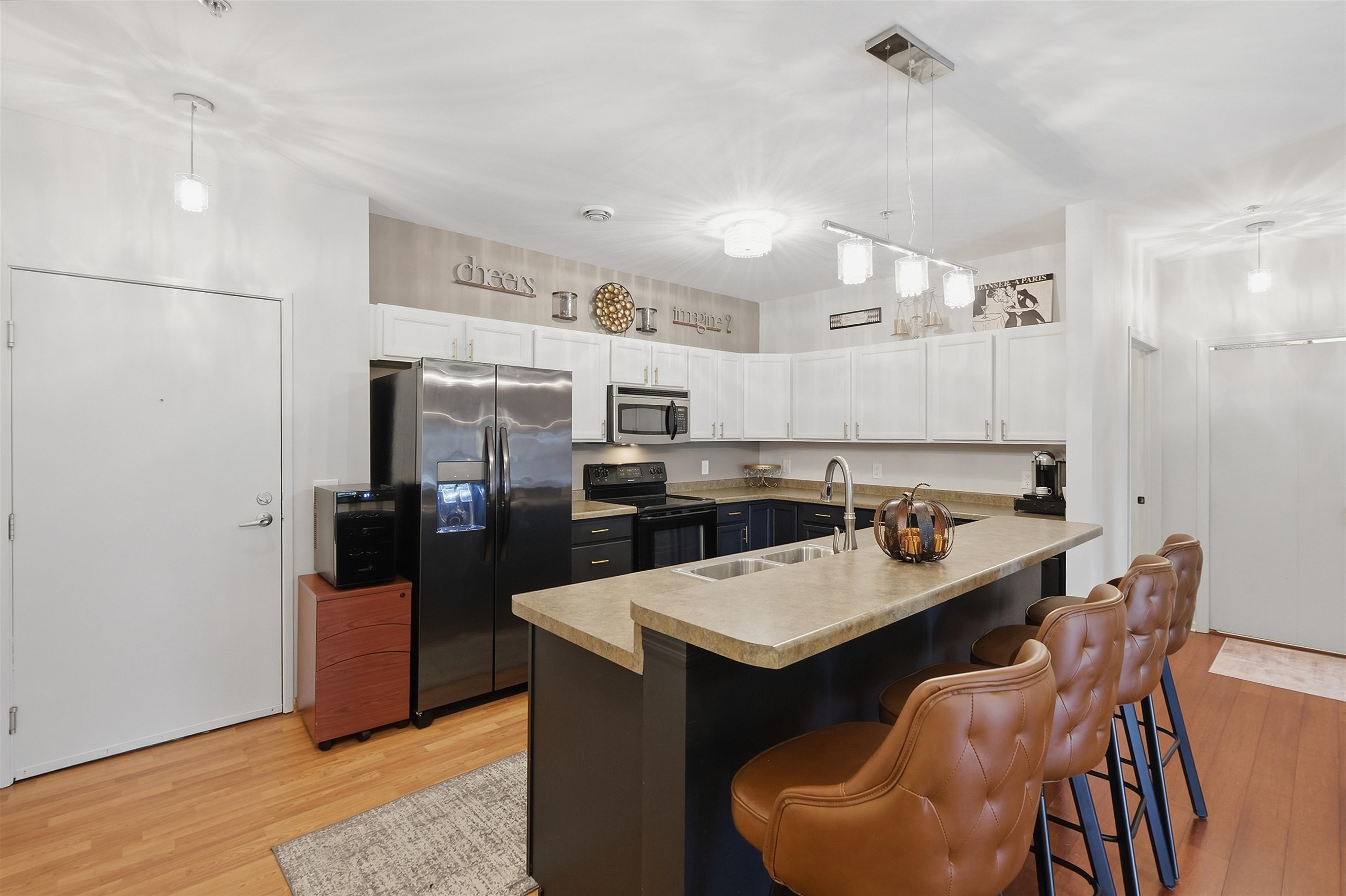 Kitchen with a large stone island, double sink, brown bar stools, and stainless steel appliances.