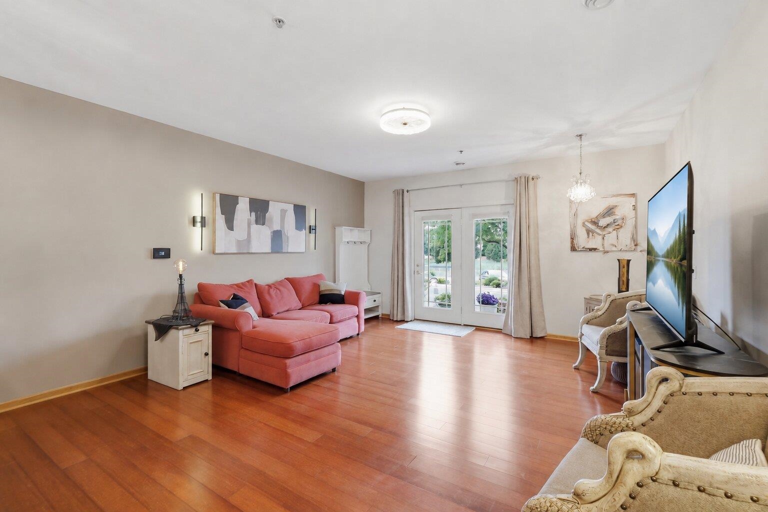 Furnished living room with a coral sectional, hardwood floors, and glass double doors.
