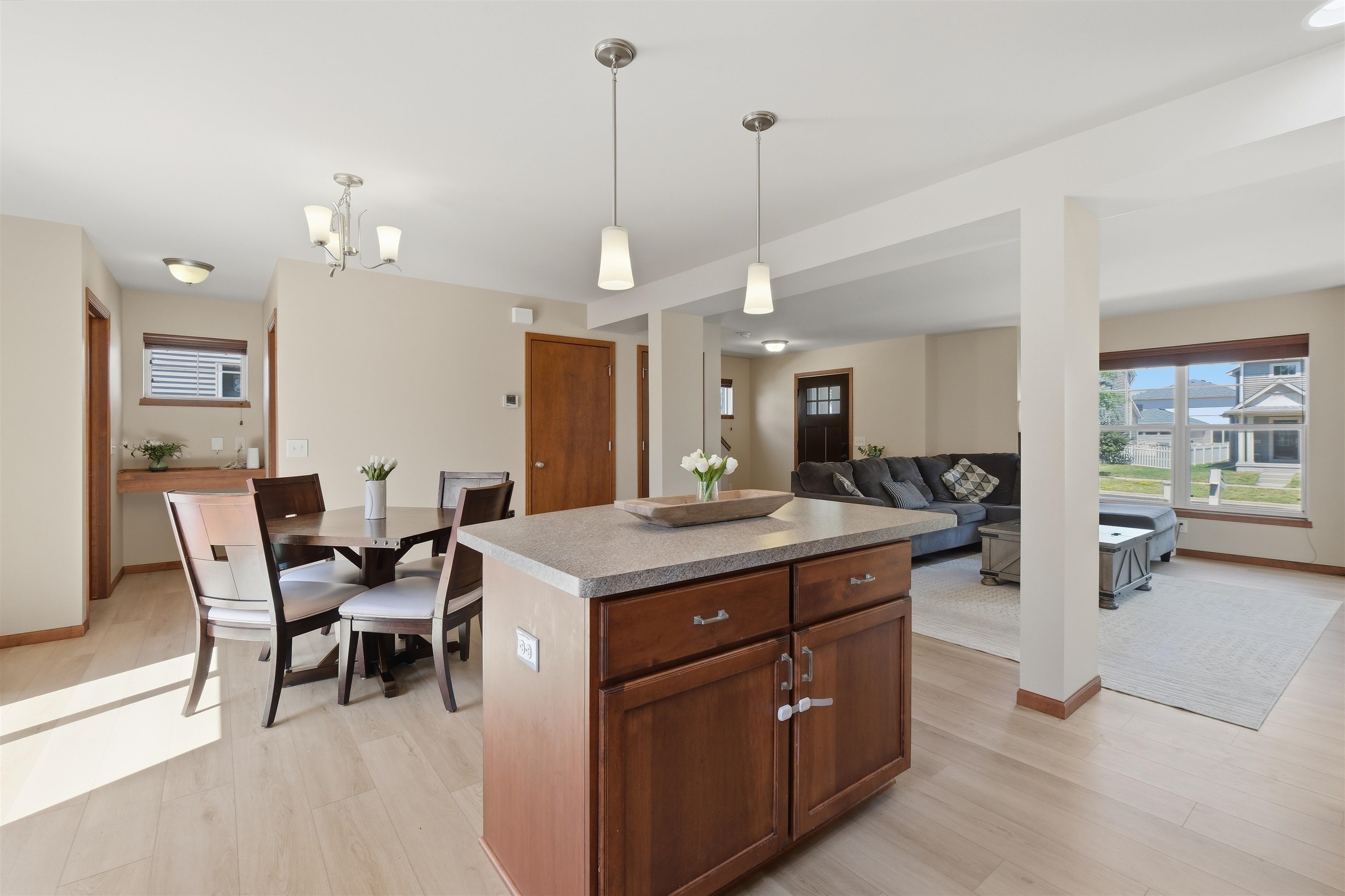 Open-plan kitchen with a large granite island, dining table, and adjoining living room with gray sectional.