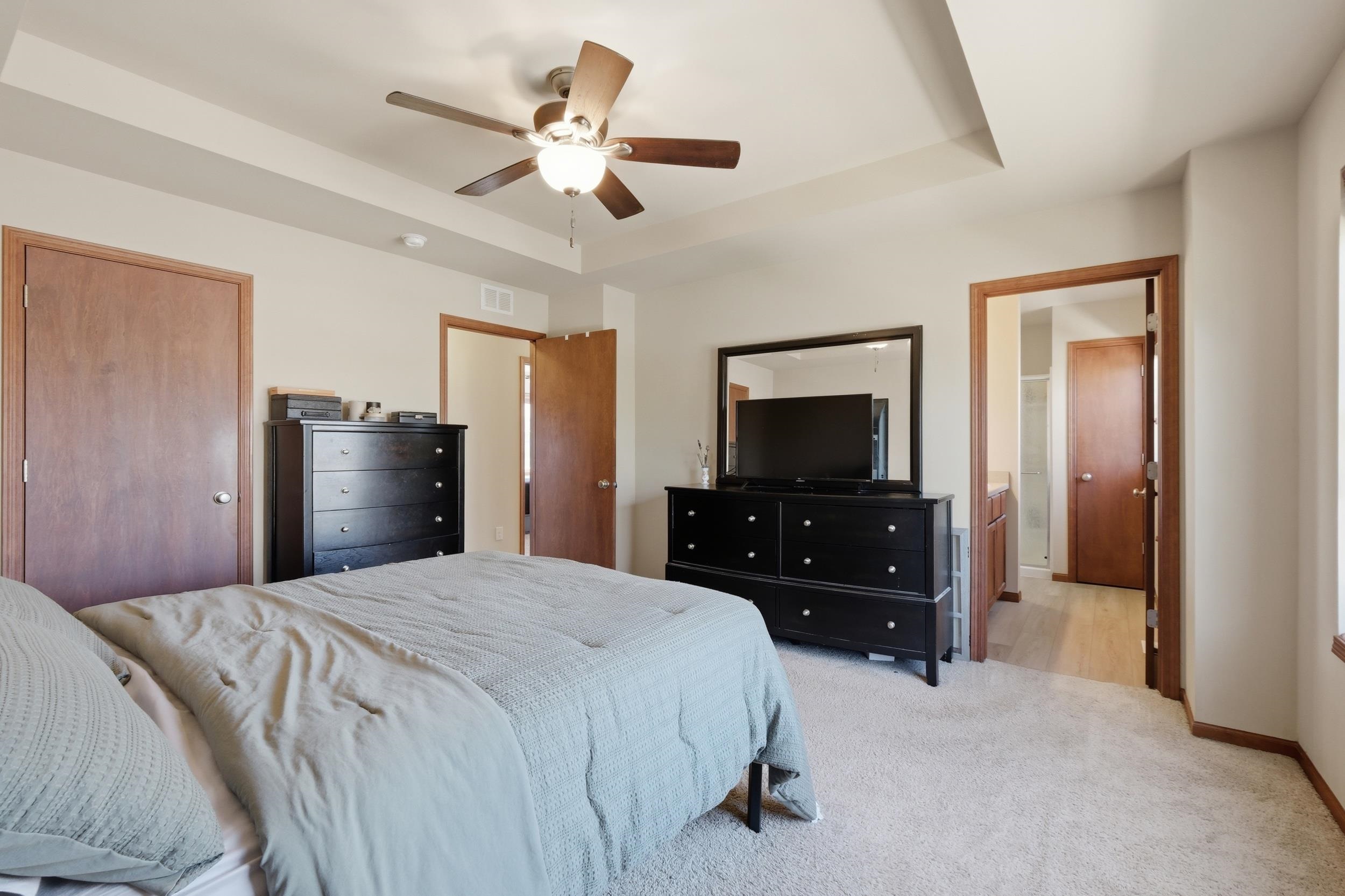 Bedroom with pale blue bedding, dark dressers, a TV and mirror, and a wood-blade ceiling fan.