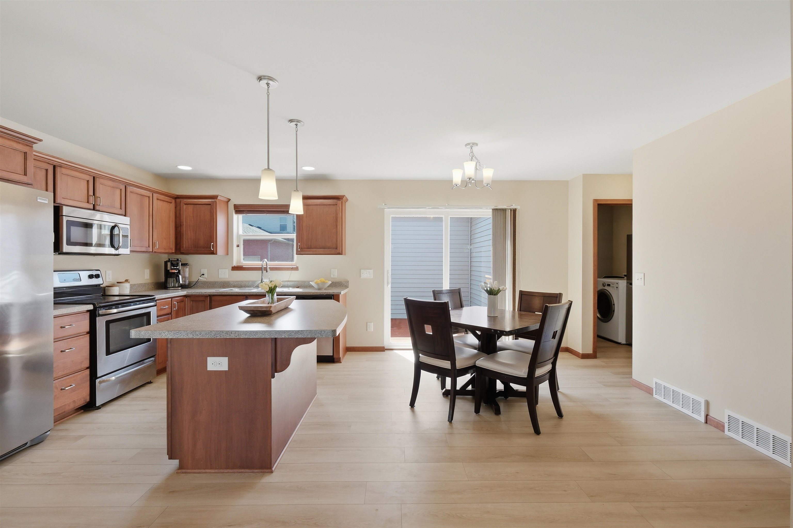 Kitchen and dining area with a large island, wood cabinets, stainless appliances, and a table by sliding doors.
